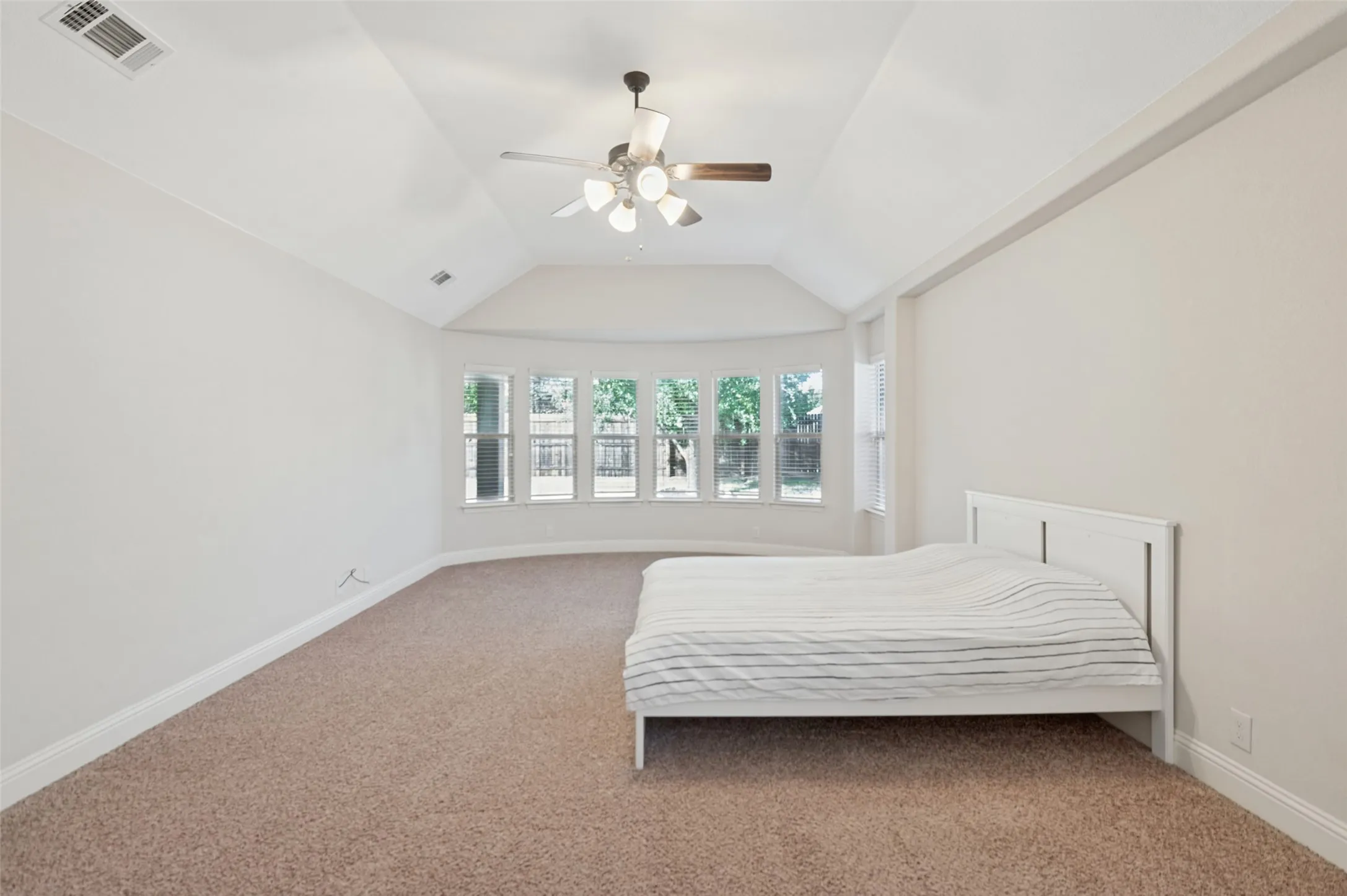 Vaulted ceiling with an attached ceiling fan and light fixture, bay window feature, and wall-to-wall carpeting