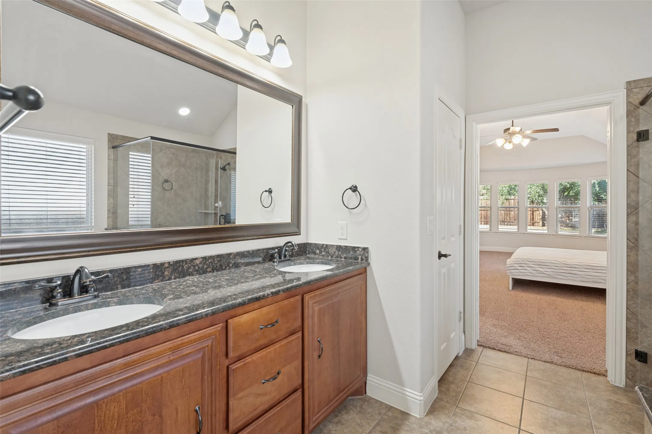 Dual vanity with dark stone countertop, wood-finish cabinetry, and framed mirror