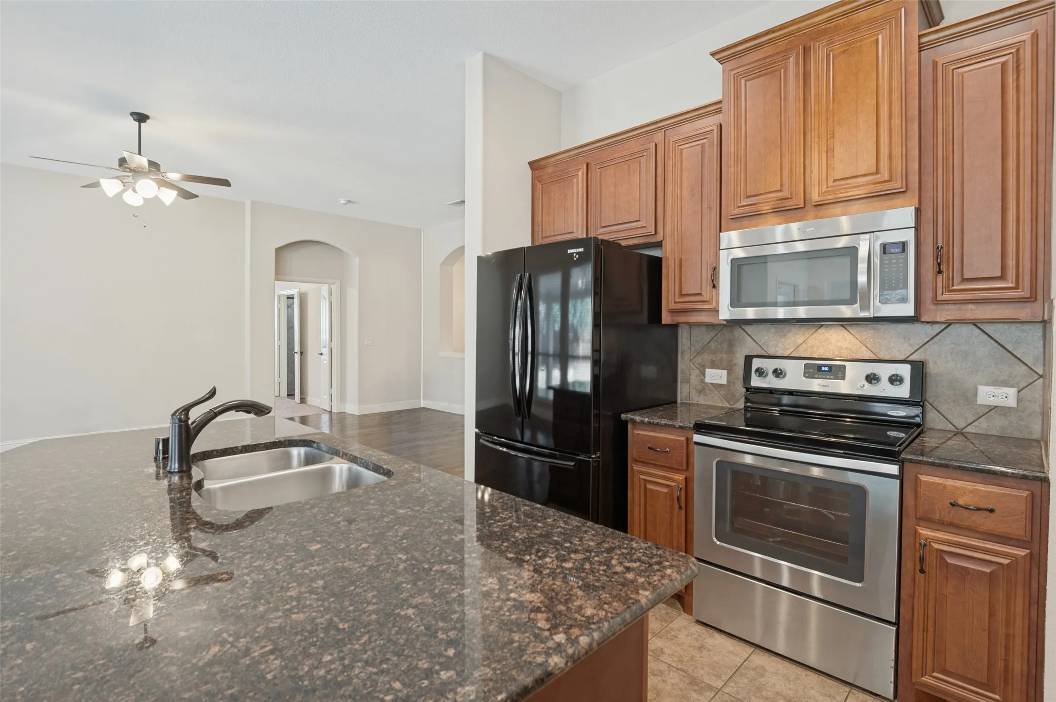 Kitchen featuring wood cabinetry, stainless steel appliances, a tile backsplash, and a large island with an undermount sink and dark countertop