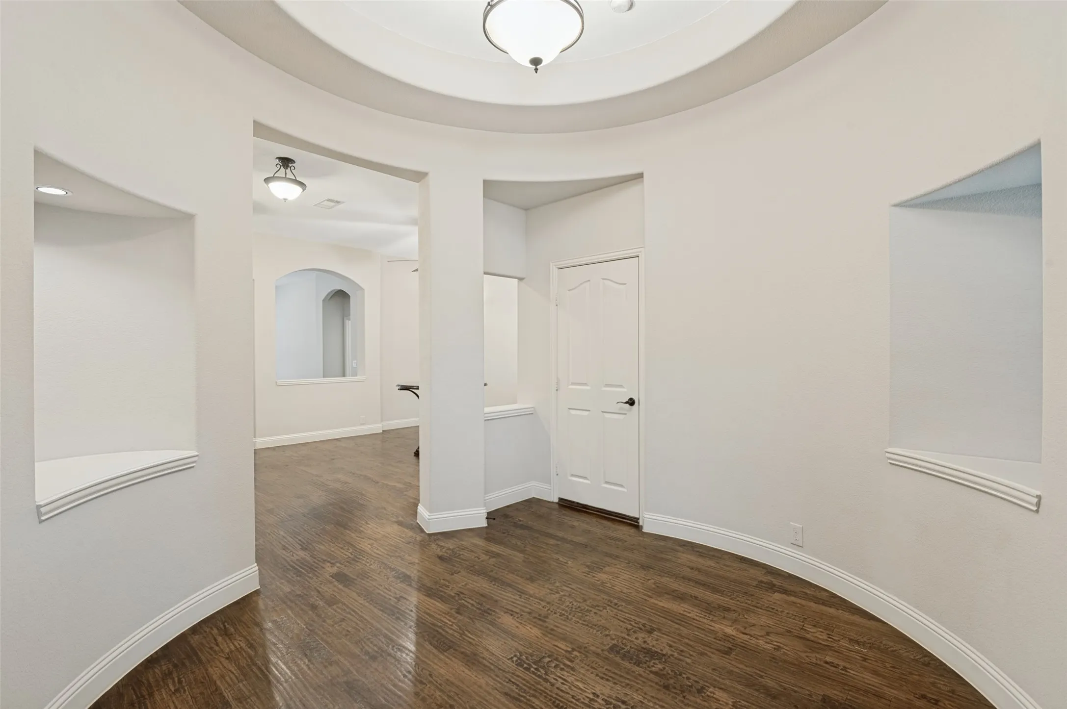 Curved architectural walls with built-in display niches, wood-finish flooring, and recessed lighting
