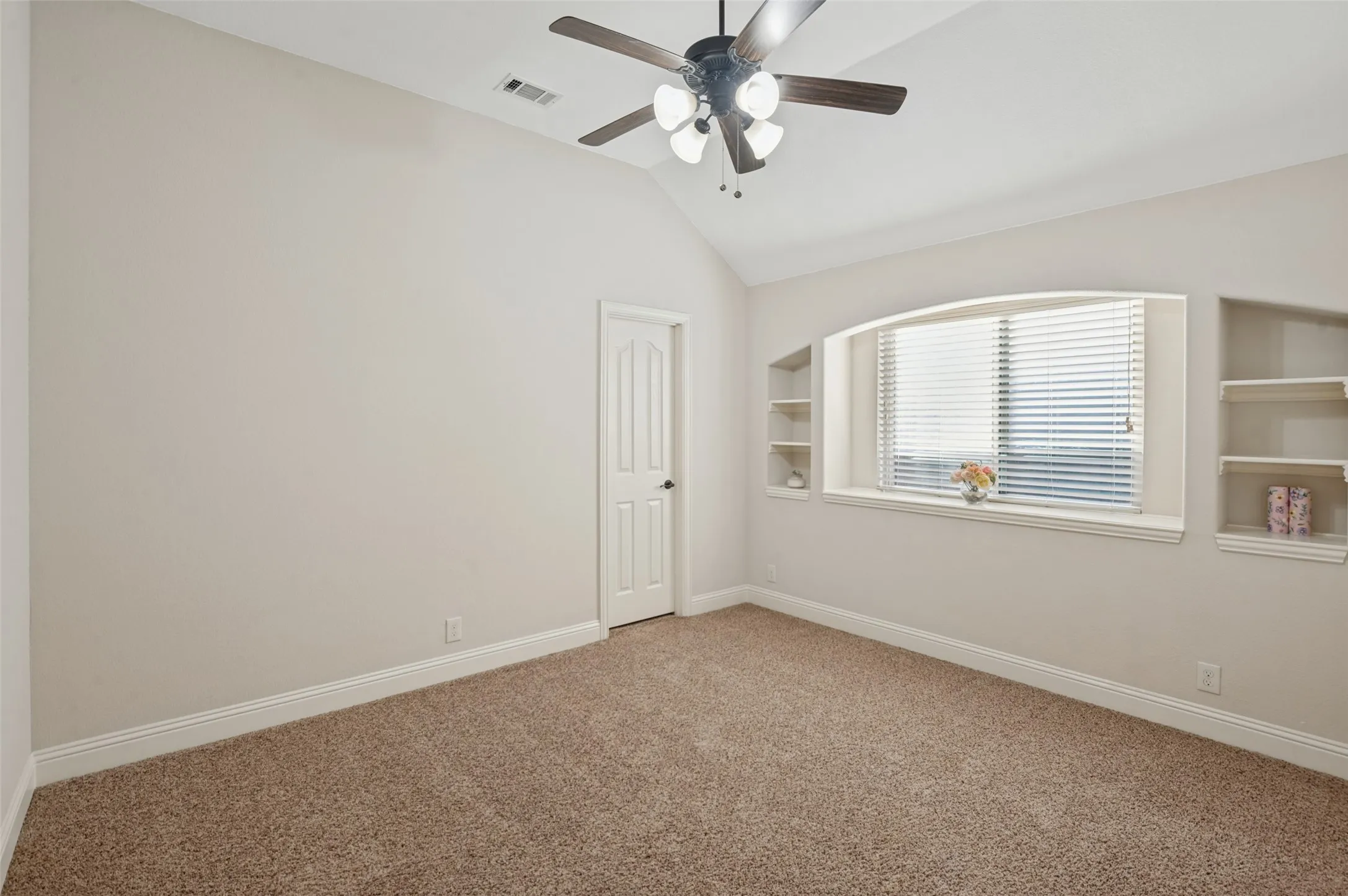 Vaulted ceiling with a ceiling fan, arched window with blinds, built-in shelving, paneled door, and carpet flooring