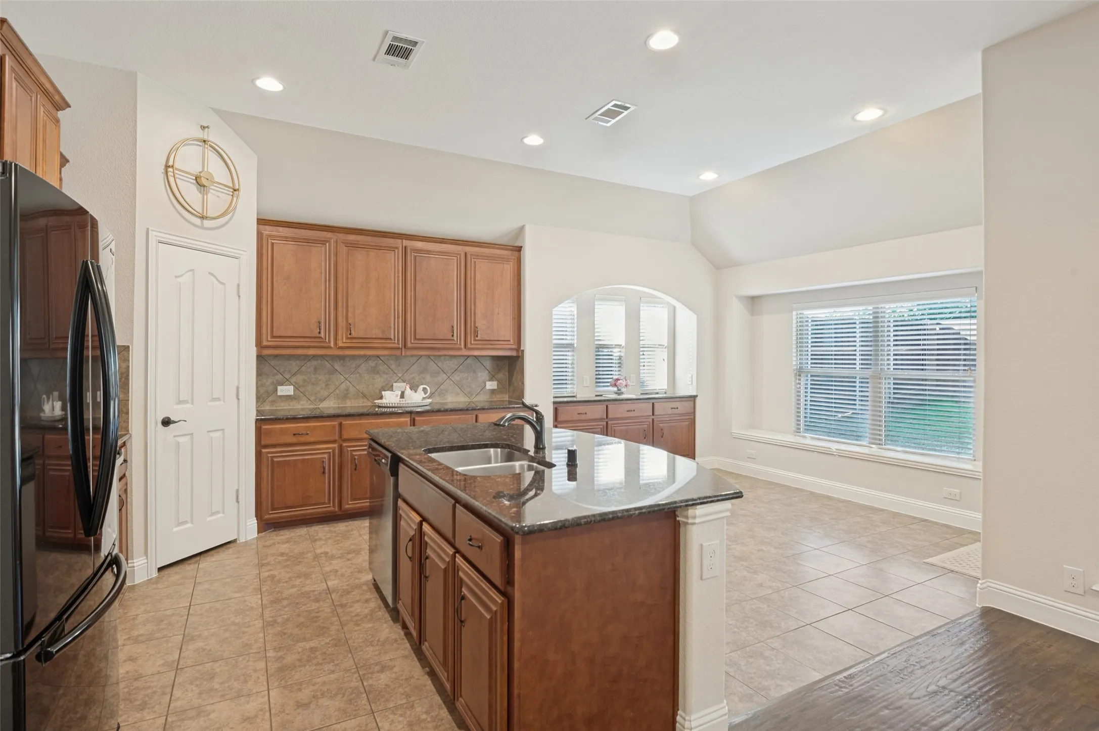 Kitchen featuring a center island with sink, extensive cabinetry, tile flooring, and vaulted ceiling
