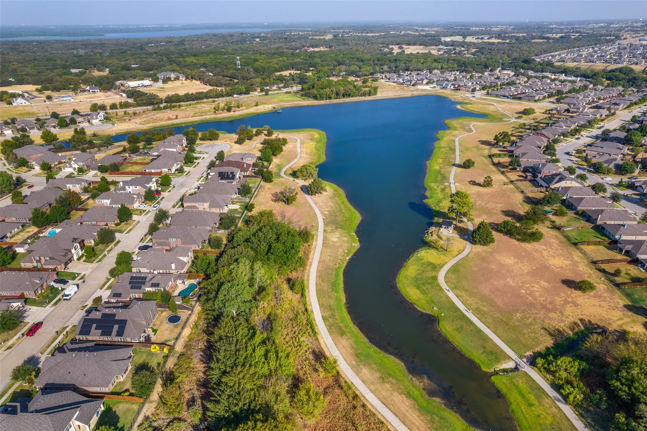 Residential development featuring a large central pond, surrounding green spaces, and paved walking paths
