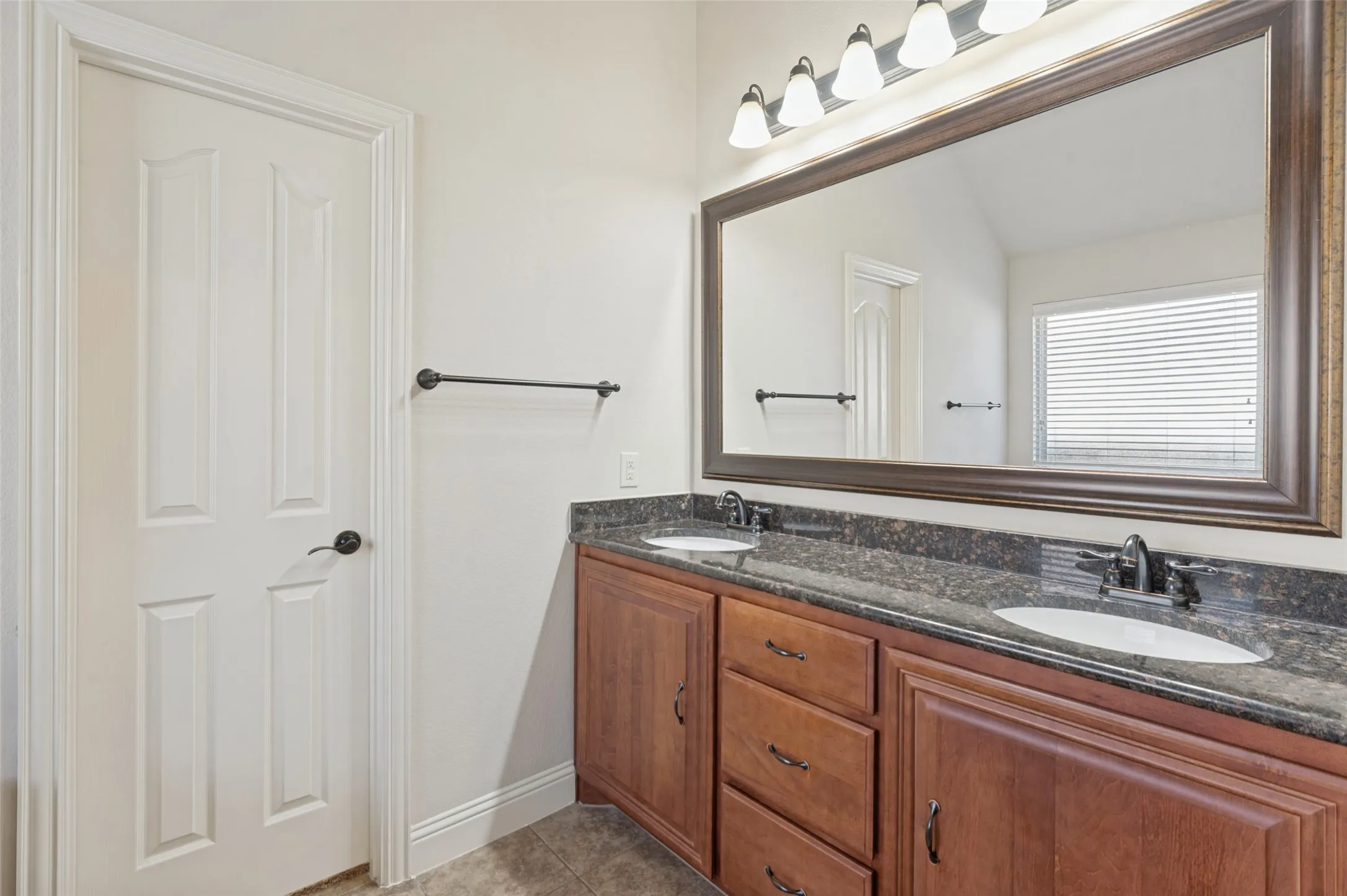 Double vanity with dark countertops, dual undermount sinks, and wood-finish cabinetry