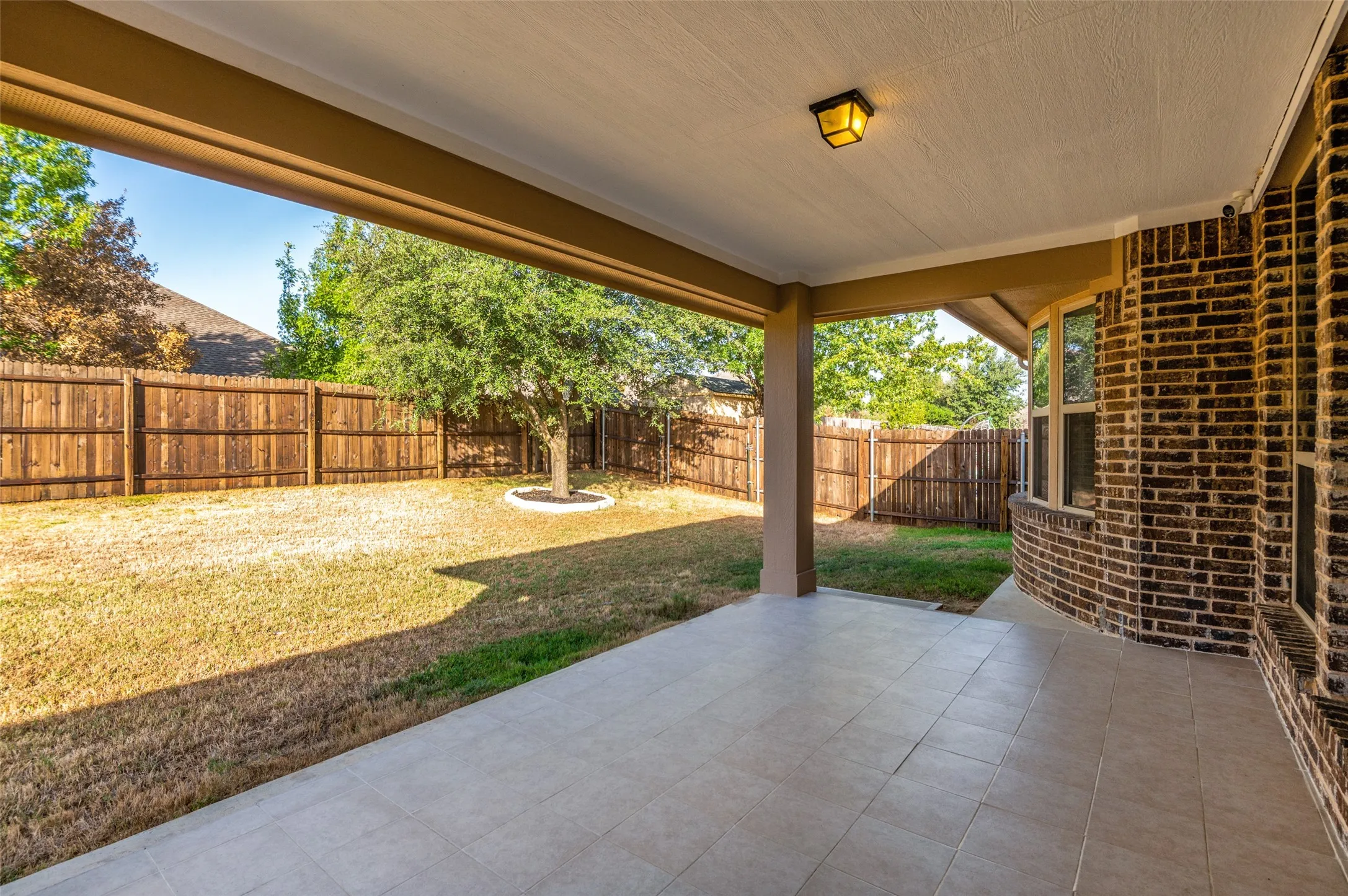Covered patio with tile flooring, brick exterior, and a privacy fence