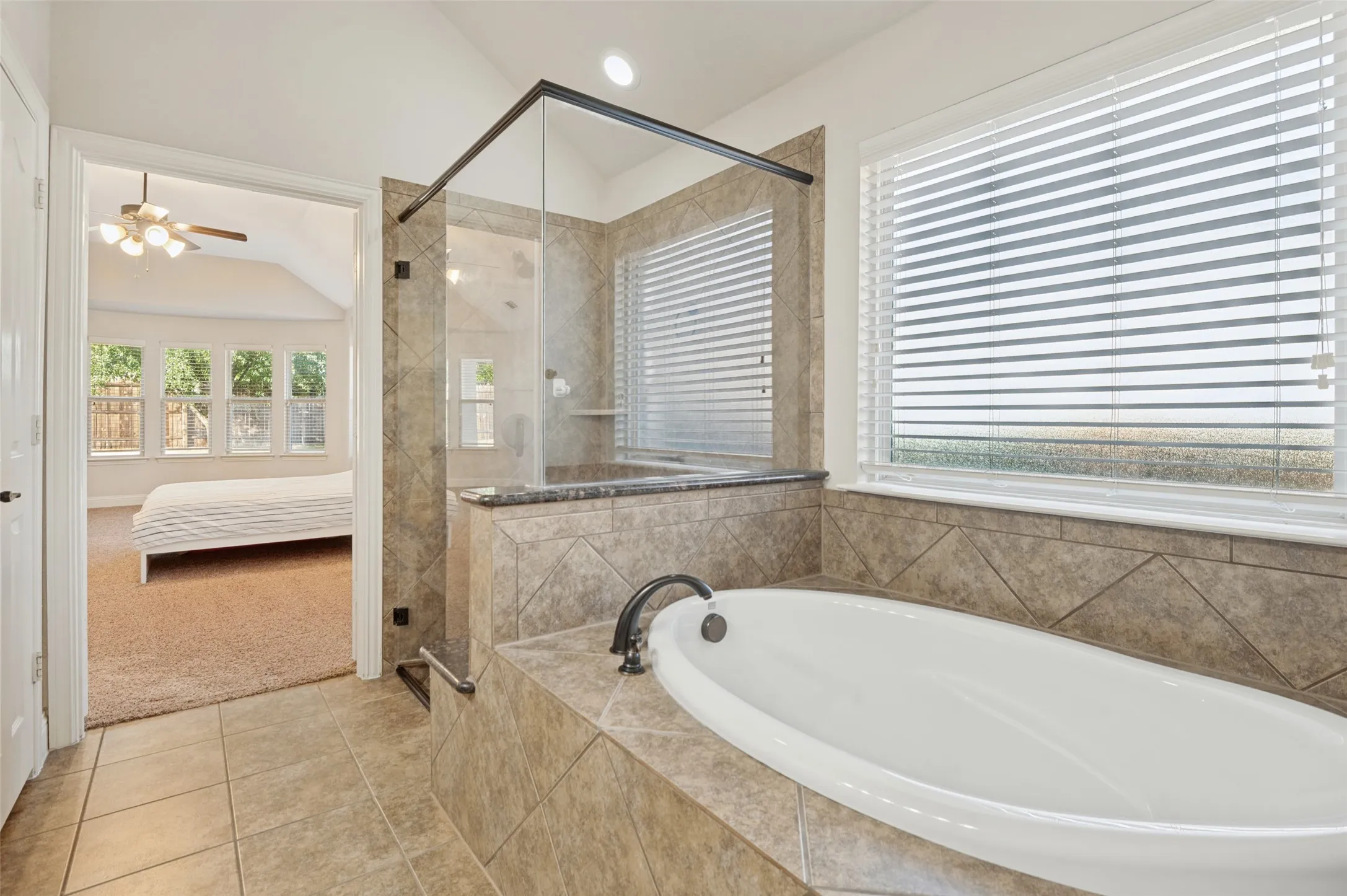 Soaking tub with a dark bronze faucet, tile surround, and a clear glass shower enclosure