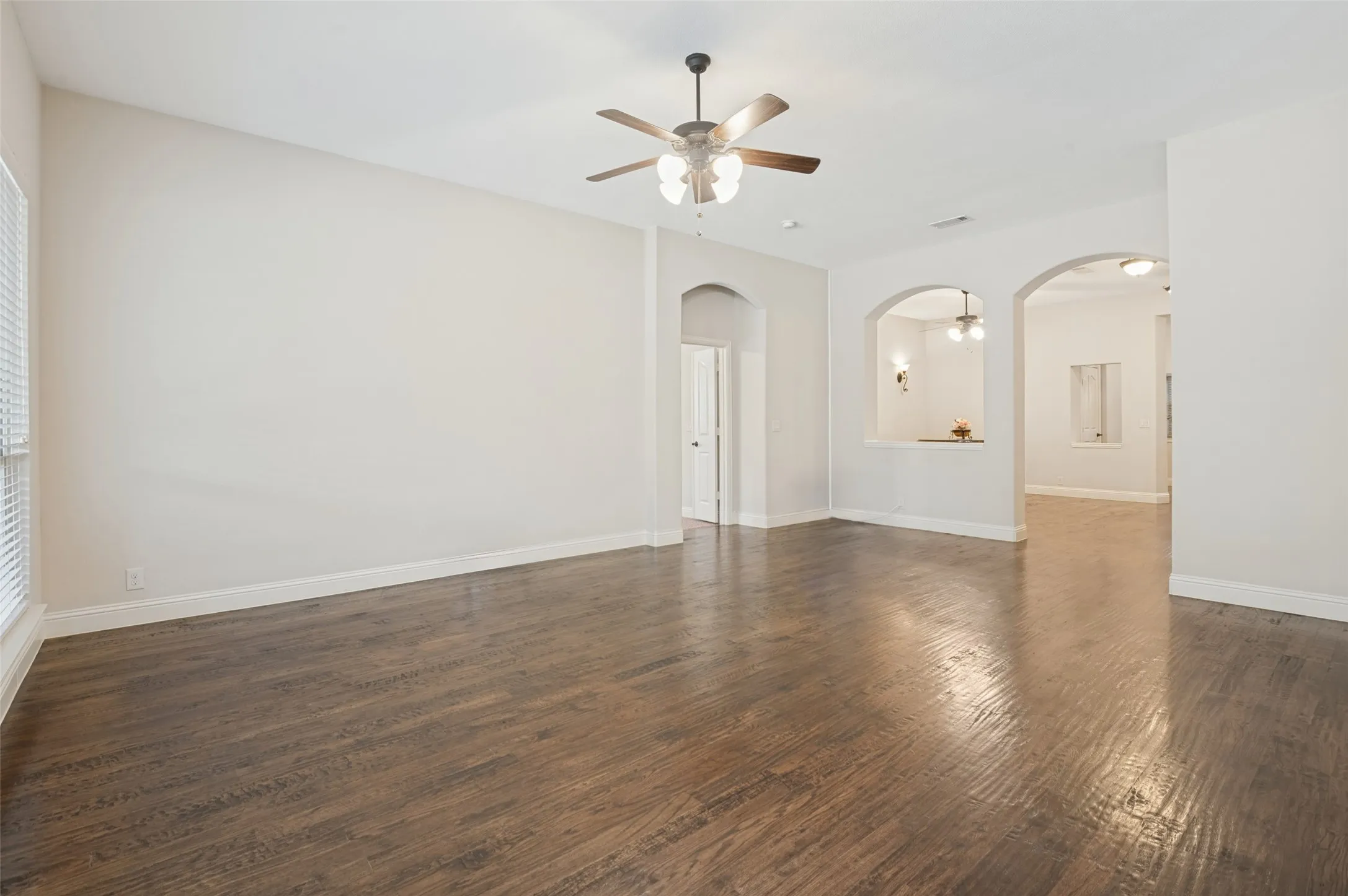 Expansive room featuring wood-finish flooring, a ceiling fan with integrated lighting, and multiple arched doorways