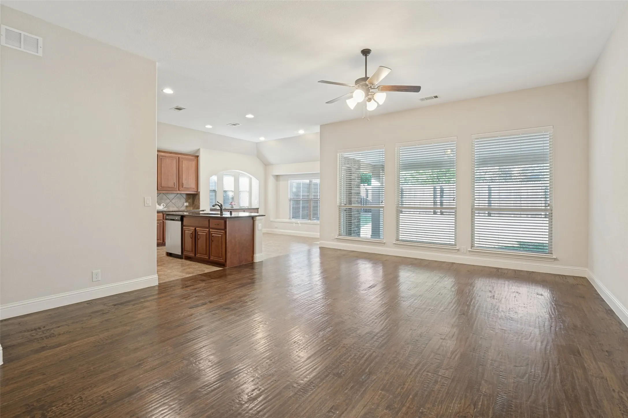 Spacious living area featuring wood-finish flooring, recessed lighting, and multiple windows with horizontal blinds