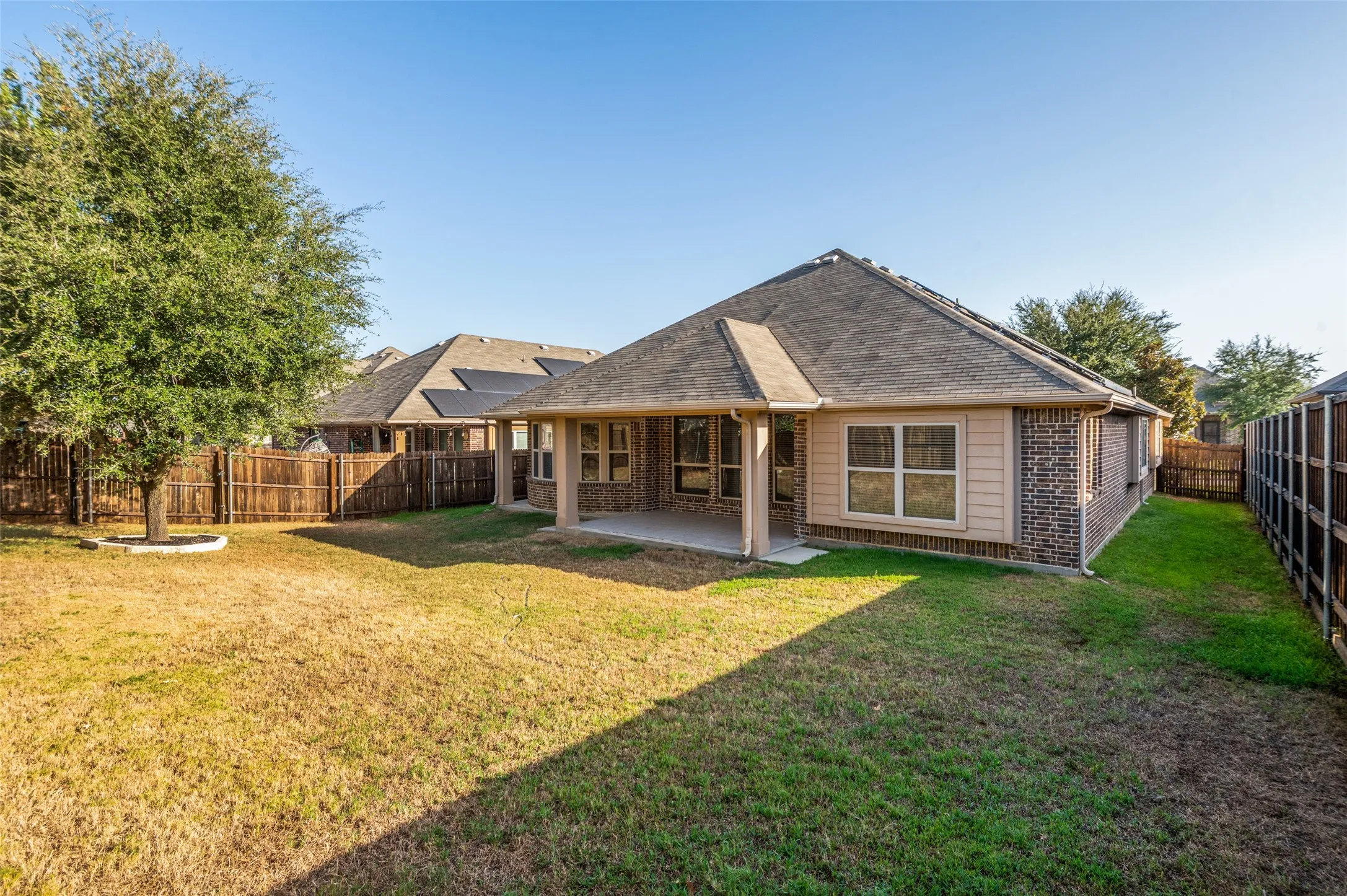 Expansive backyard featuring a covered patio, wood fencing, and mature trees