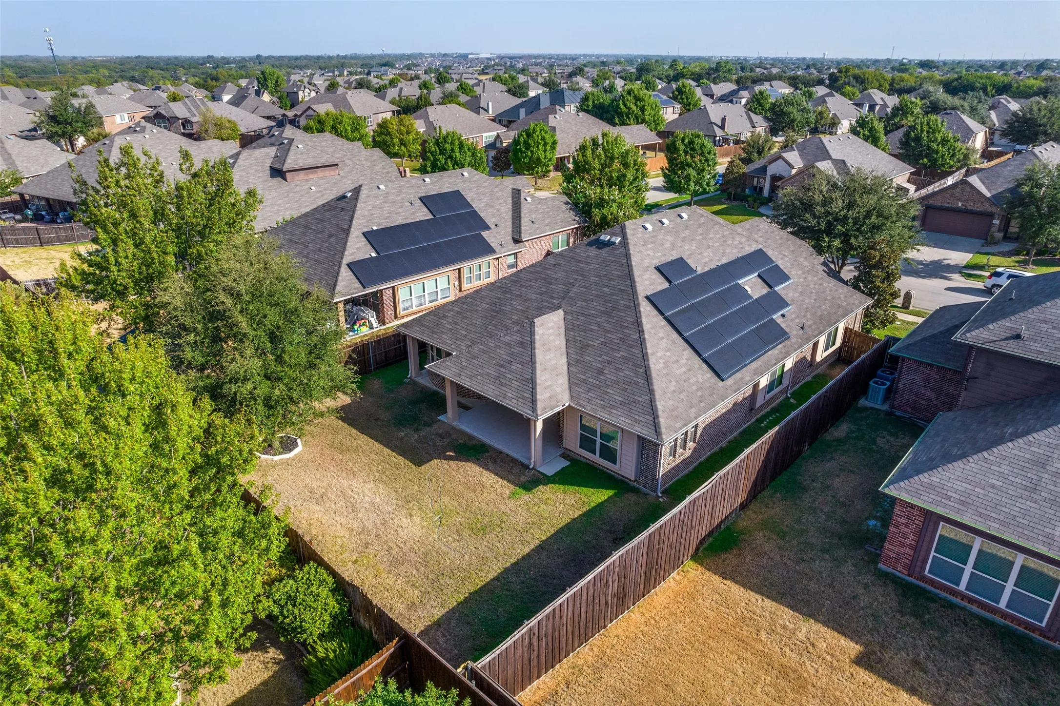 Roof-mounted solar panels, covered patio, fenced backyard, and brick exterior