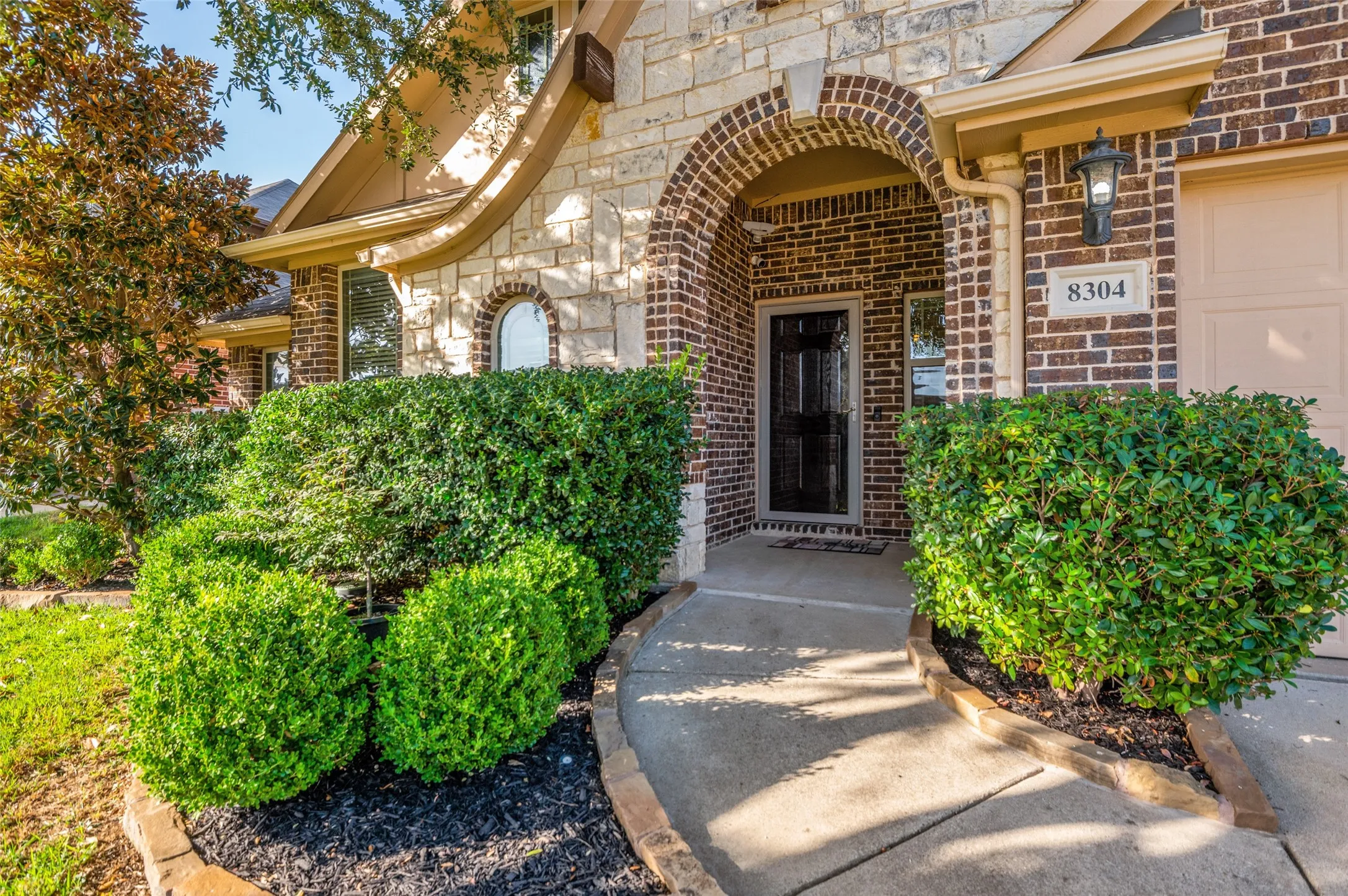 Brick and stone facade with an arched entryway, detailed front door, and a concrete pathway