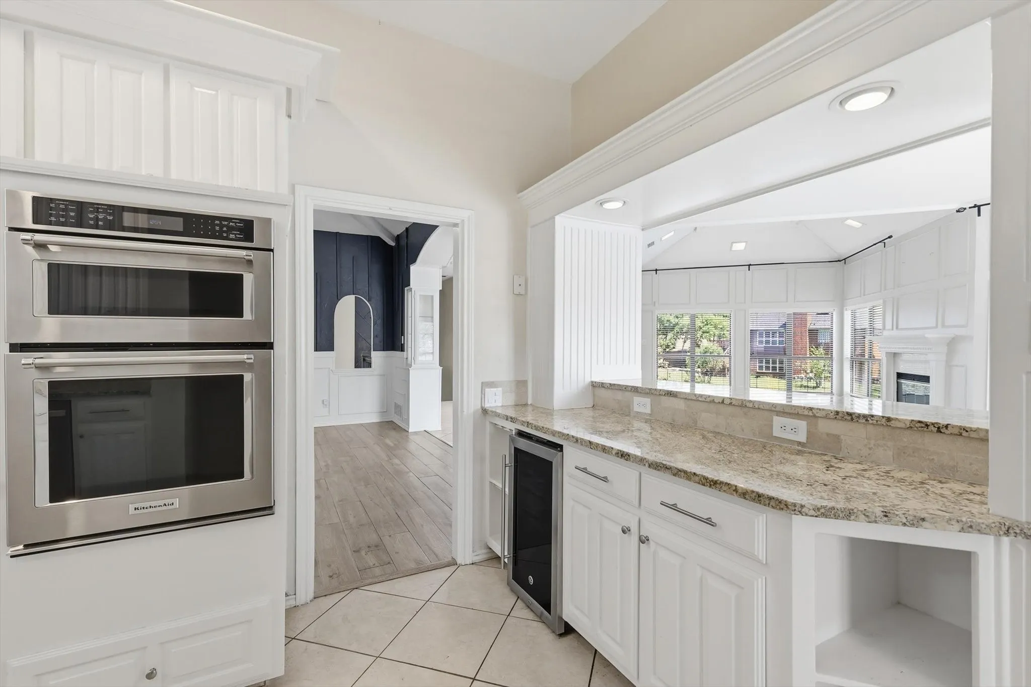 Built-in stainless steel double oven, white cabinetry, granite countertops, tile flooring, and integrated beverage cooler