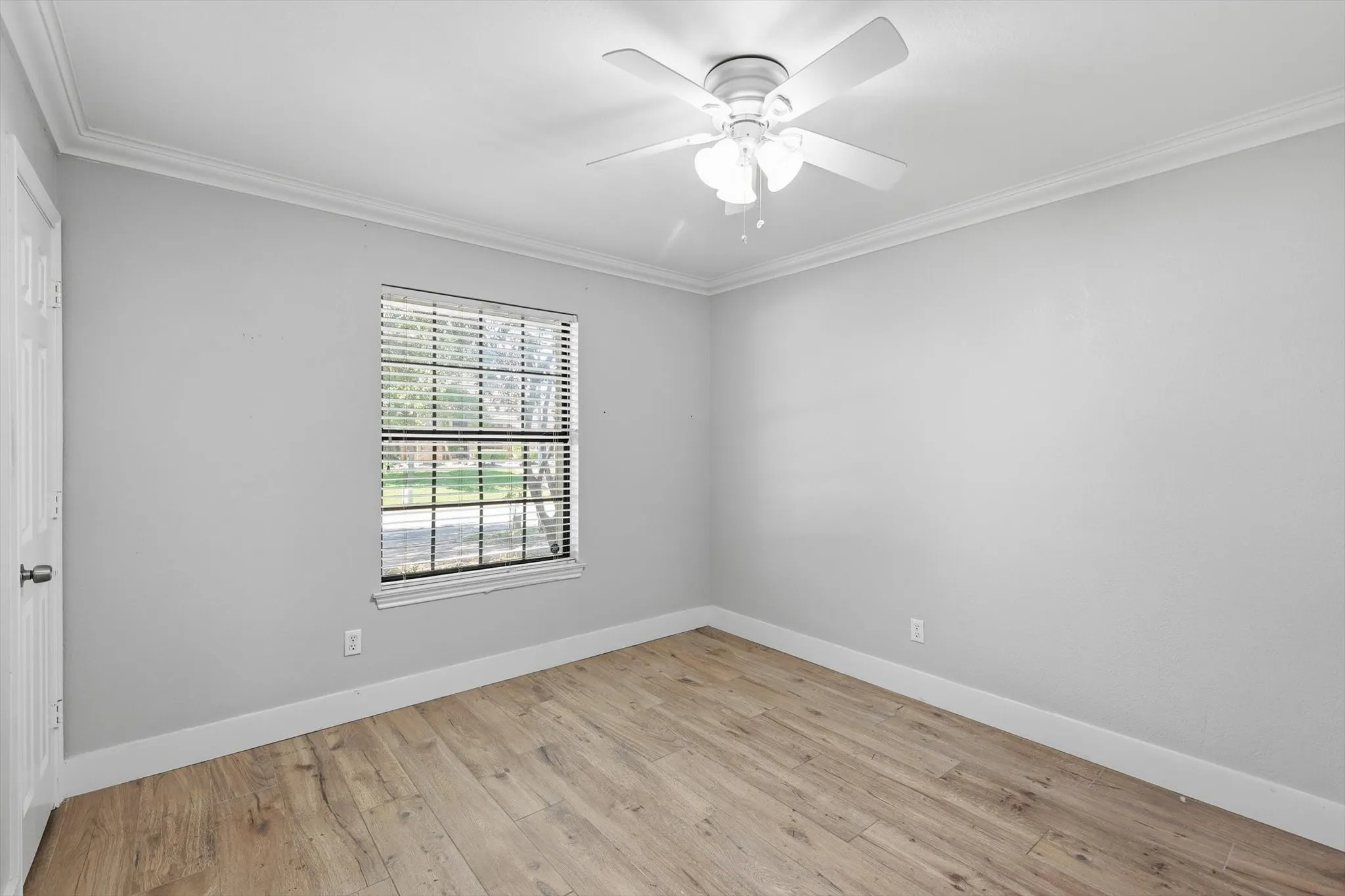 Wood-finish flooring, crown molding, ceiling fan with integrated lighting, and a single window with blinds