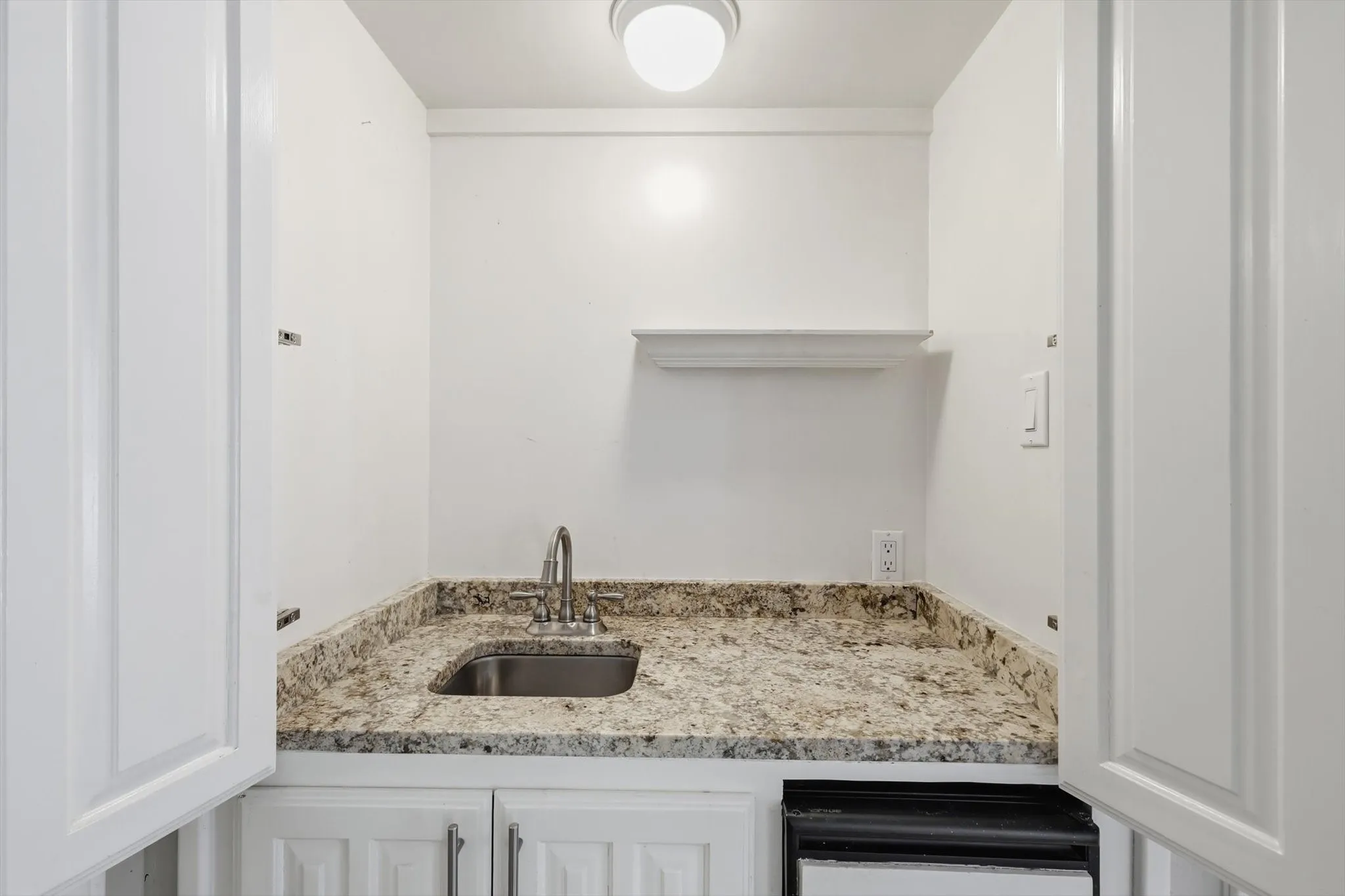 White cabinetry with brushed nickel hardware, light-toned stone countertop, stainless steel sink with a chrome faucet, and a built-in appliance