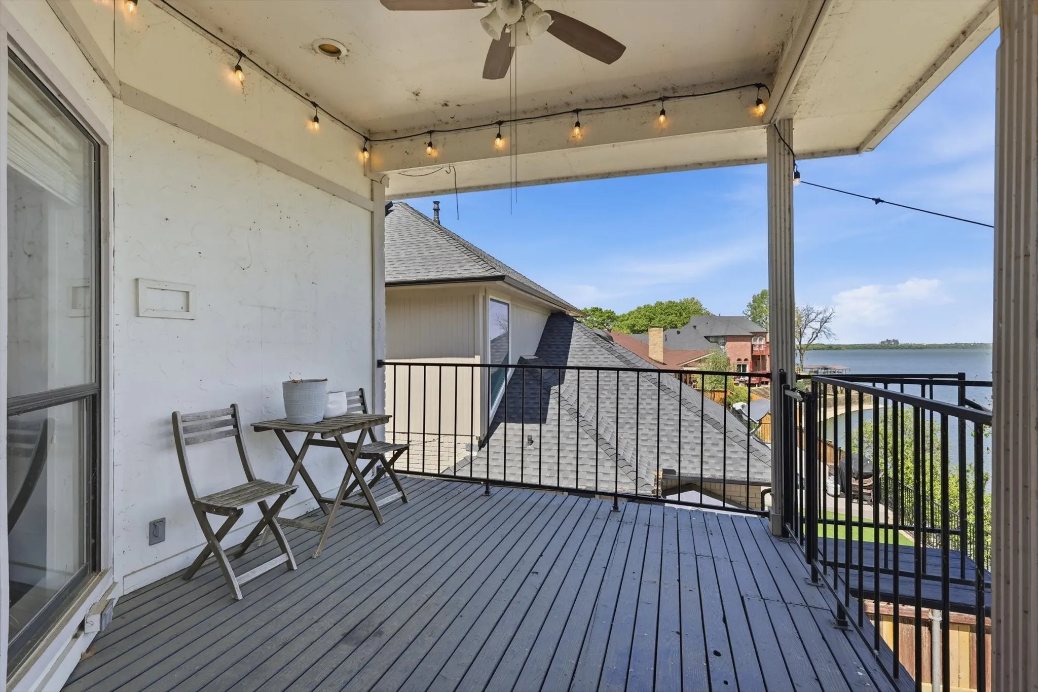 Elevated deck with a ceiling fan, string lighting, and black metal railings overlooking a body of water