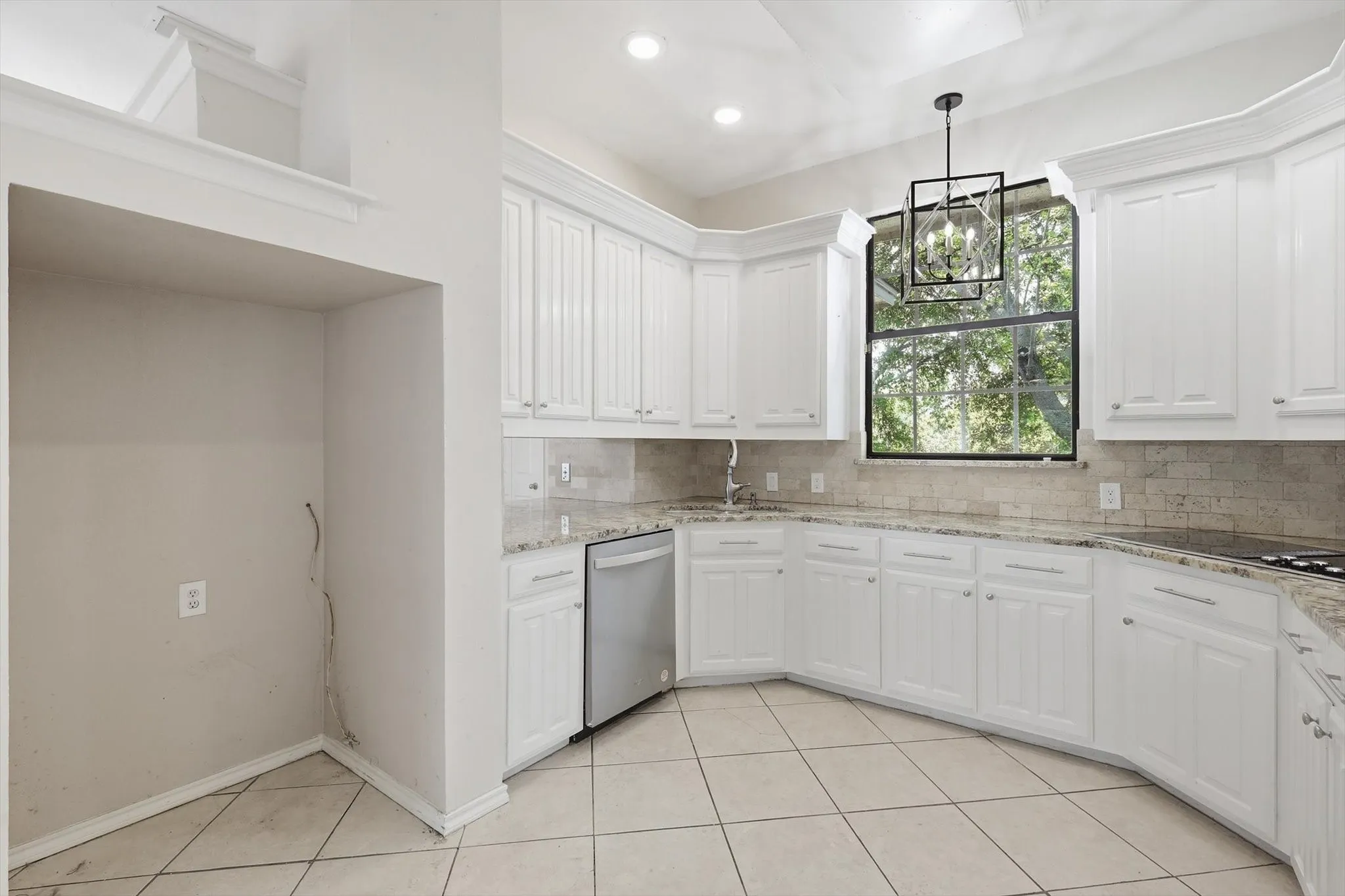 White cabinetry, stone countertops, integrated dishwasher, tiled flooring, and a contemporary chandelier