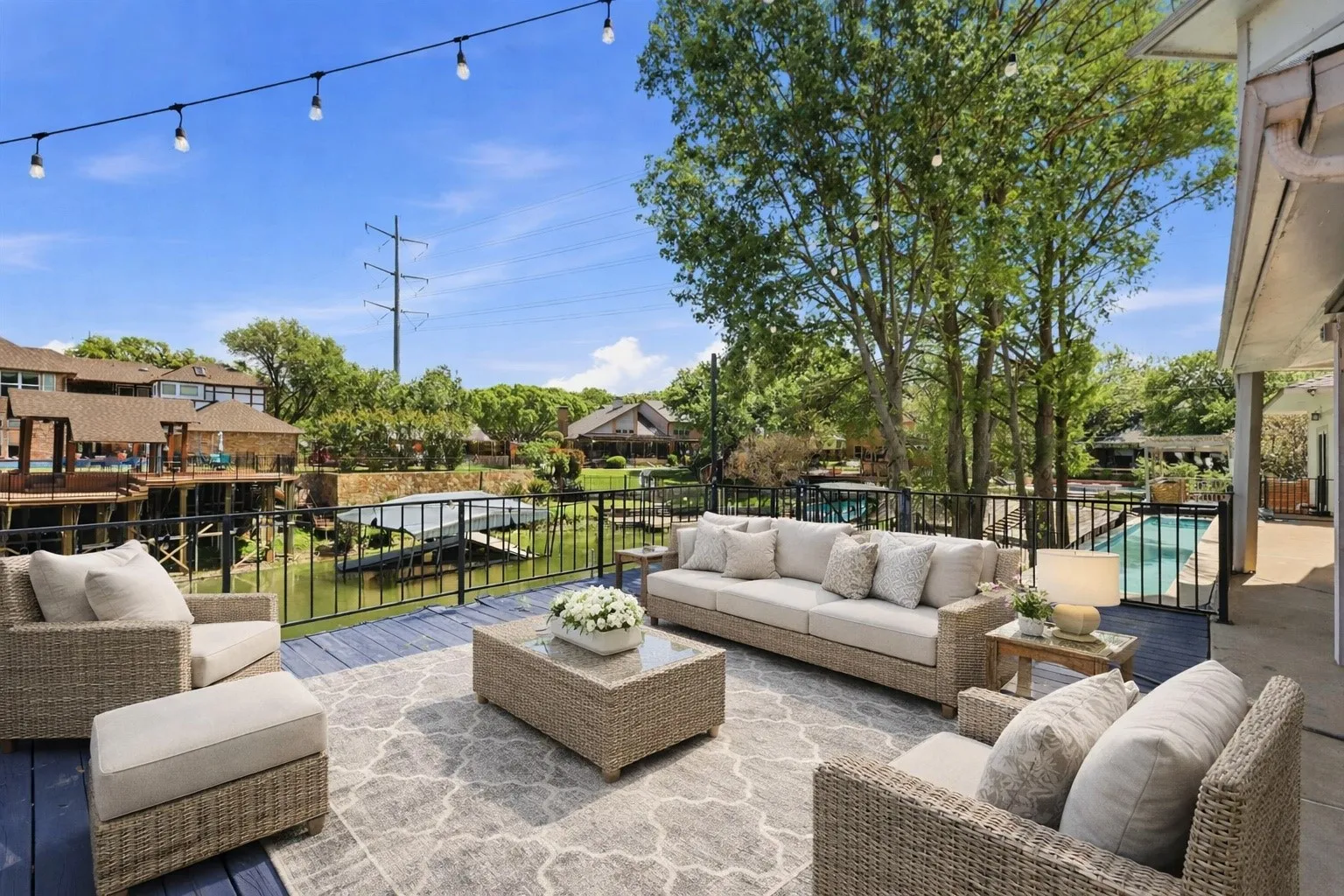 Virtually Staged. Expansive outdoor deck with string lighting, black metal railing, and water frontage