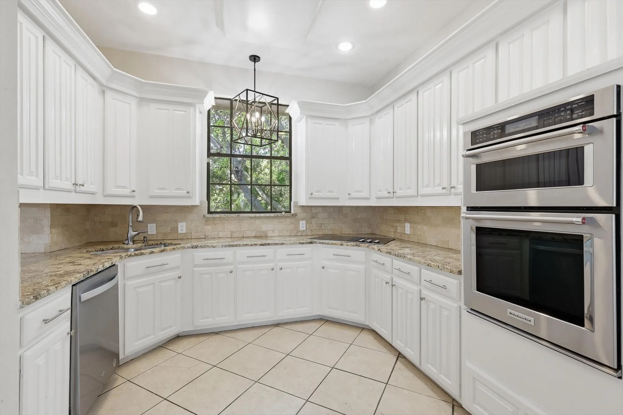 White cabinetry, built-in stainless steel appliances, light-toned tile flooring, L-shaped countertop, and stone backsplash