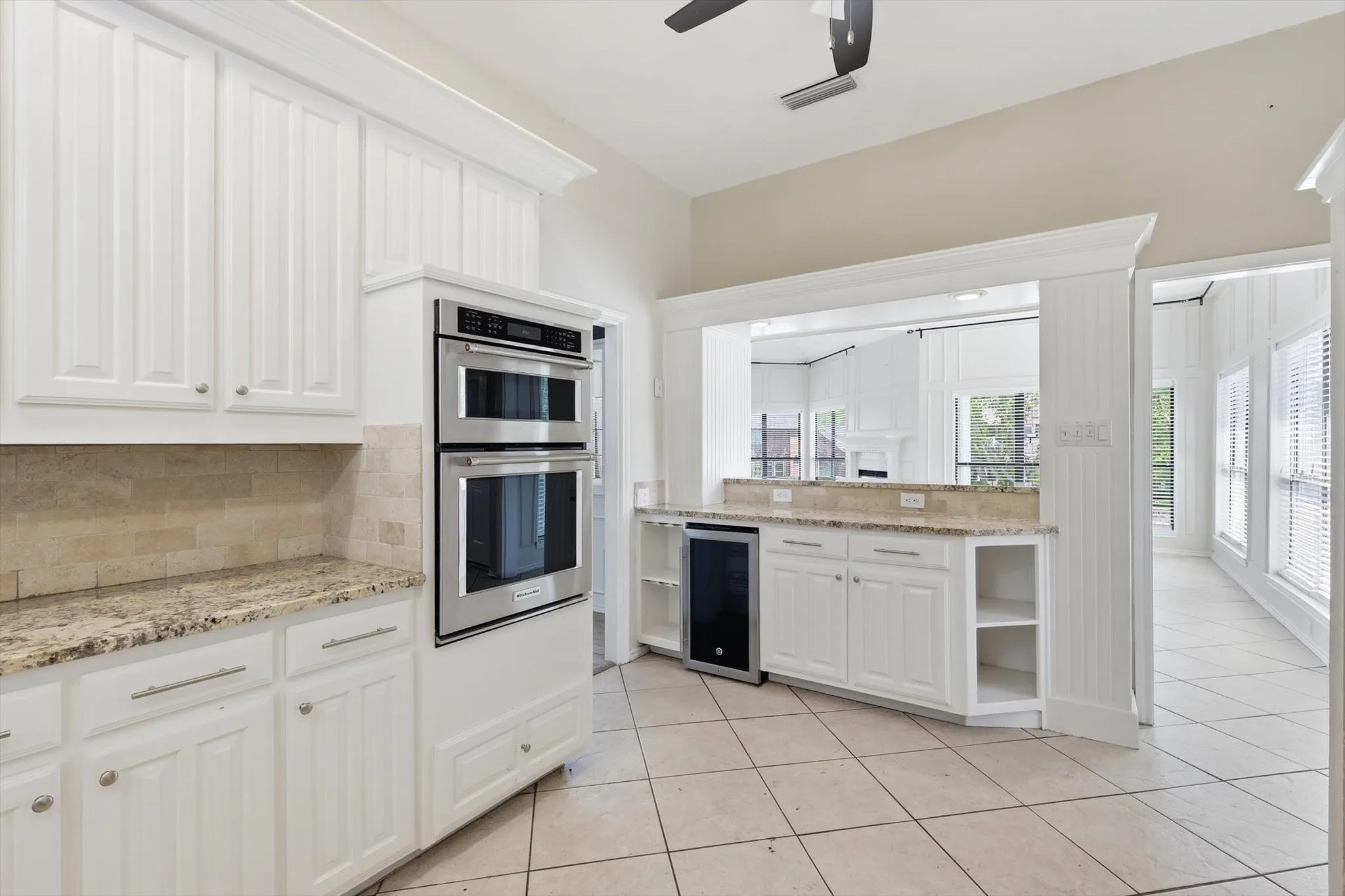 White cabinetry, double wall ovens, stone countertops, stone tile backsplash, and tile flooring