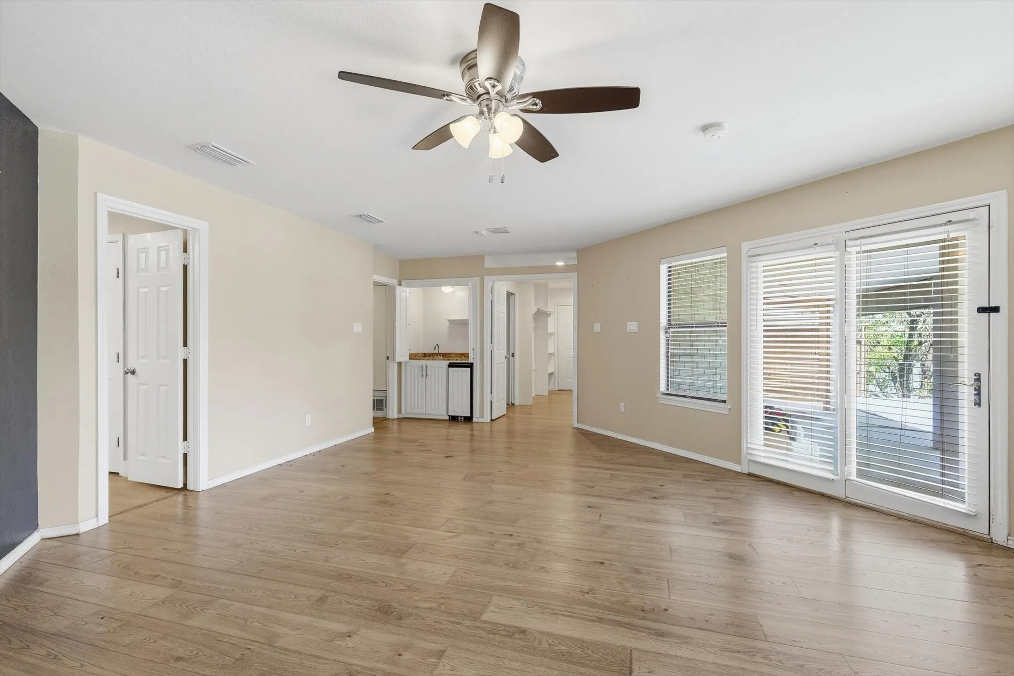 Wood-finish flooring, ceiling fan with integrated lighting, glass sliding door, and a built-in wet bar with cabinetry