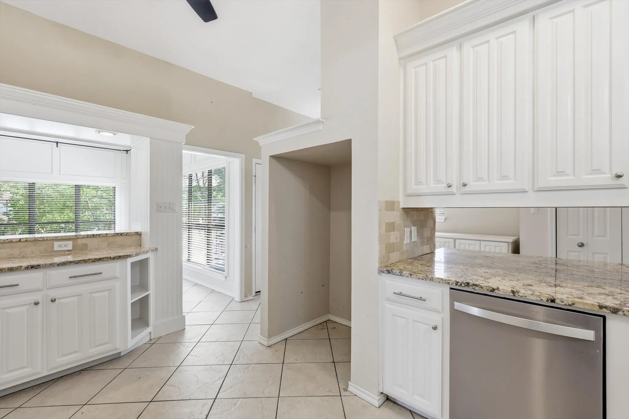 White cabinetry with crown molding, light-toned granite countertops, and a stainless steel dishwasher