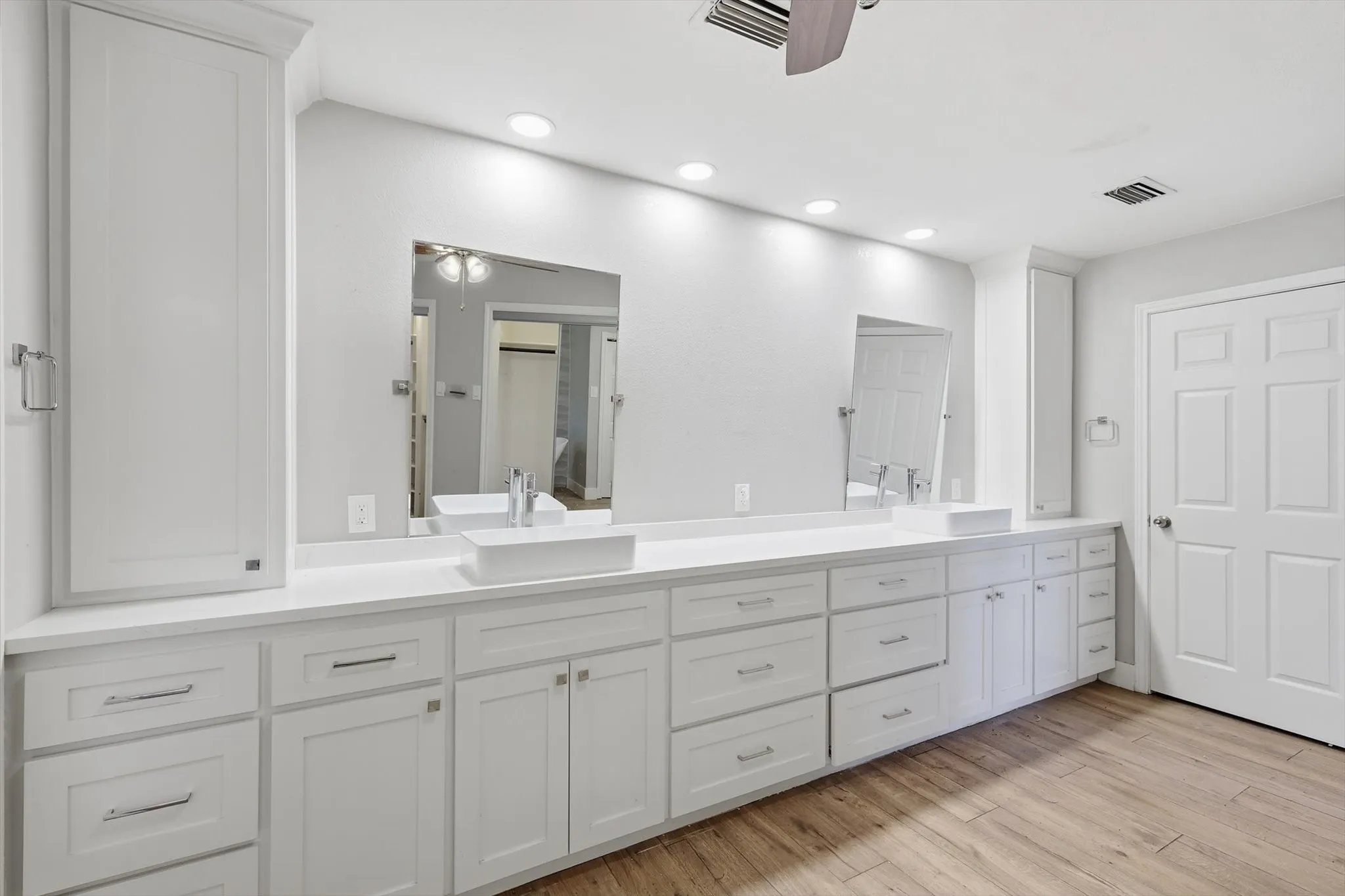 Dual vessel sinks set into an expansive vanity with white cabinetry and light-colored countertops