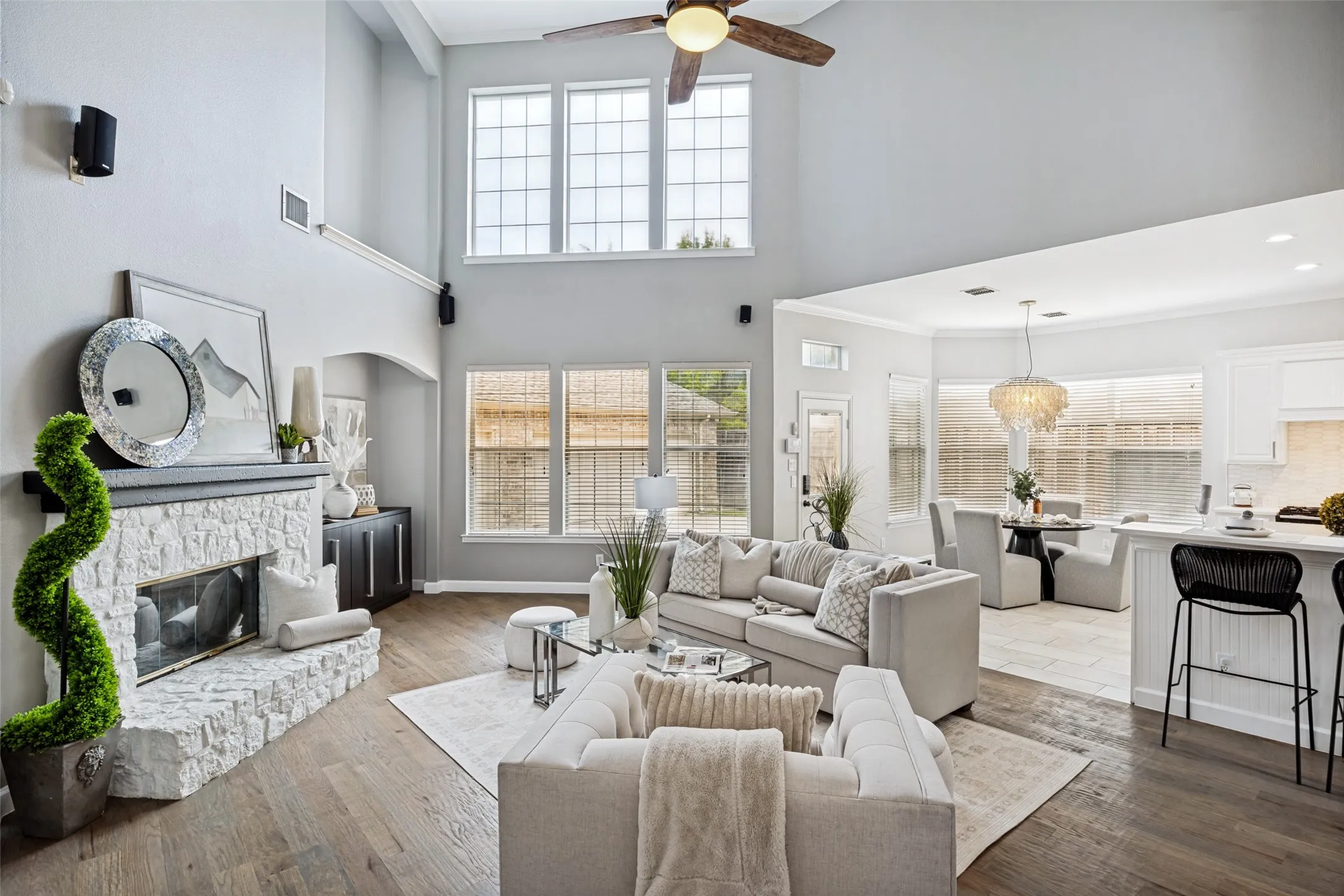 Two-story living area with high ceilings, wood-finish flooring, a stone-clad fireplace, and multiple large windows