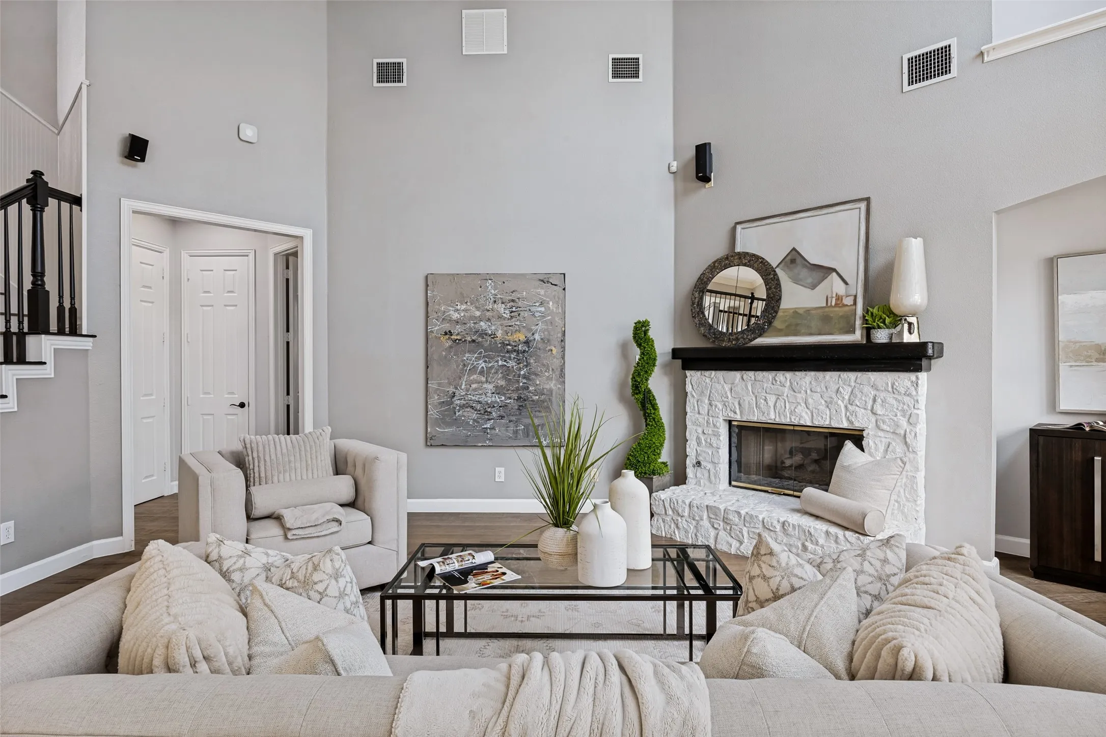 Vaulted ceiling, stone-clad fireplace with mantel, dark wood-finish flooring, and a staircase with dark balusters