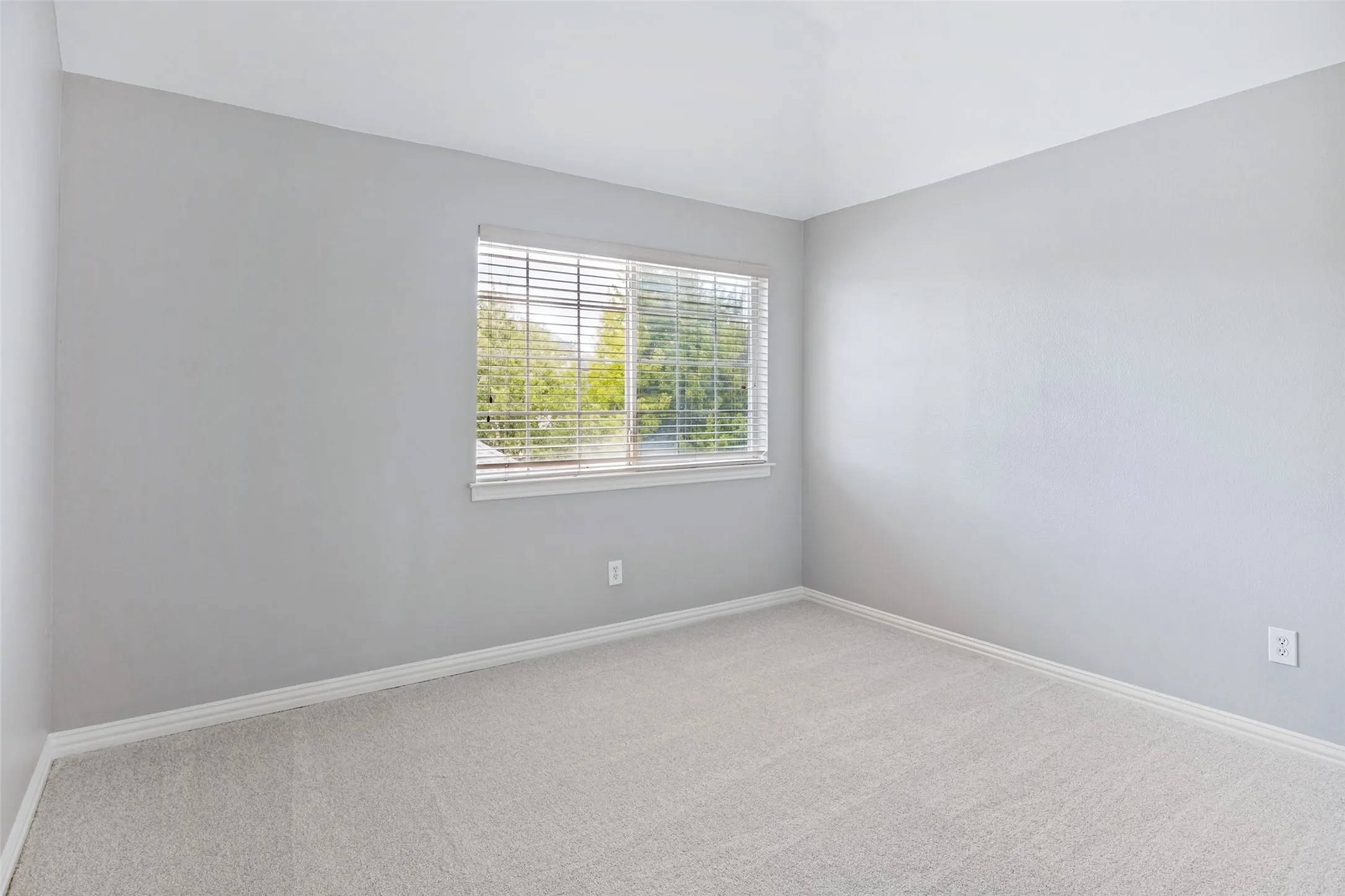 Vaulted ceiling room featuring light gray walls, white trim, and light-colored carpeting