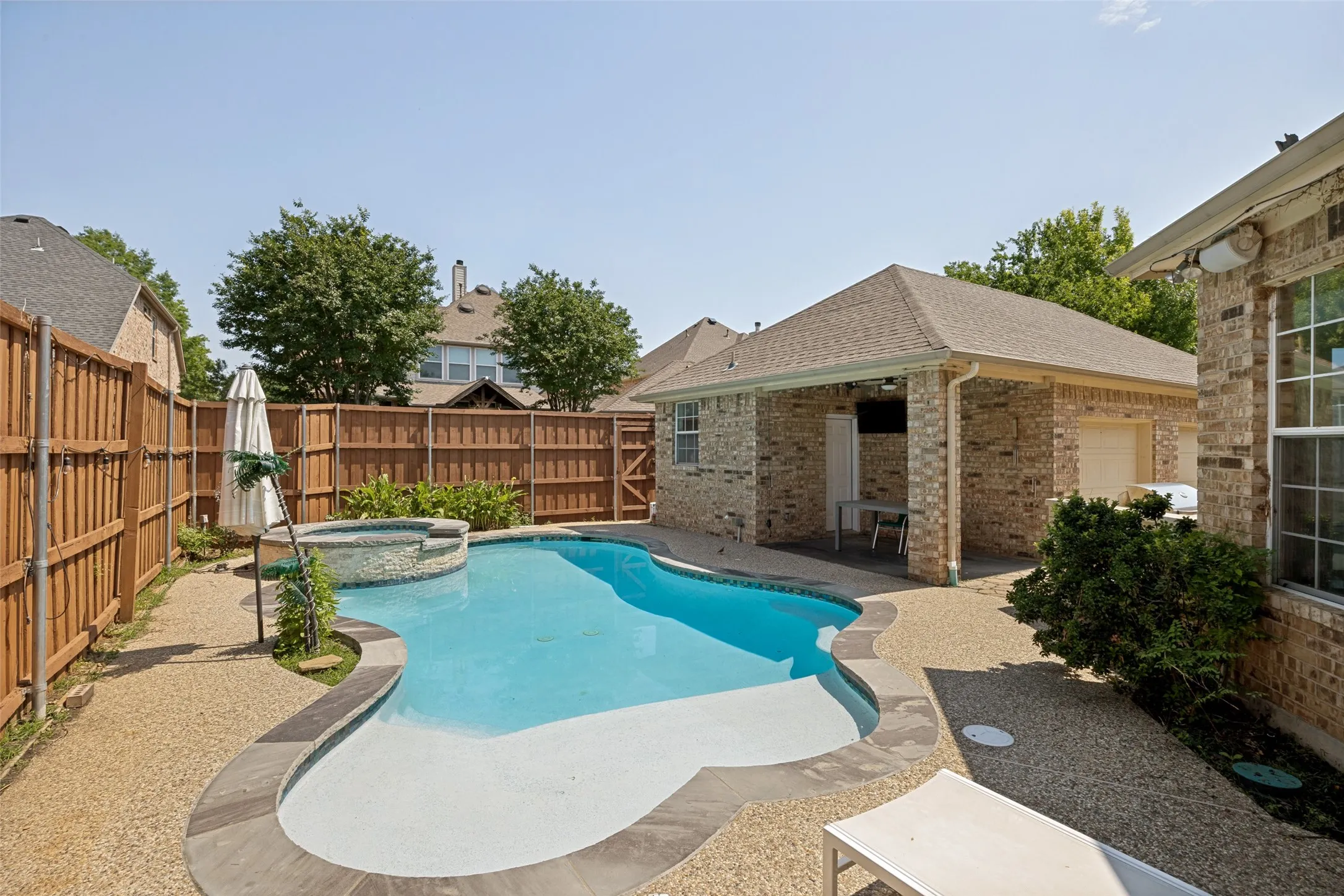 Resort-style backyard featuring a freeform swimming pool, integrated spa, covered patio, and aggregate hardscaping