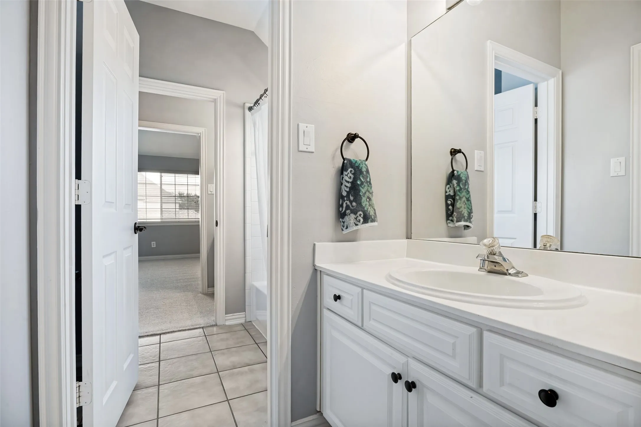 White vanity with an integrated sink and chrome faucet, tile flooring, and a full-width mirror