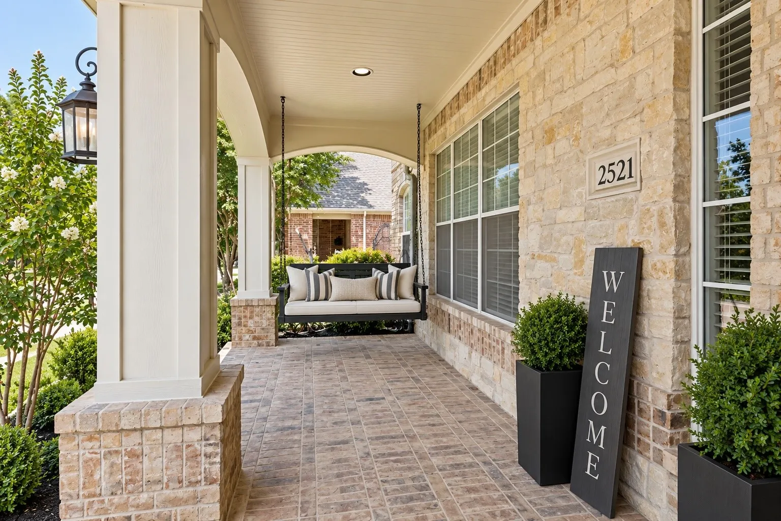 Covered front porch featuring a brick facade, white columns, a porch swing, and integrated lighting