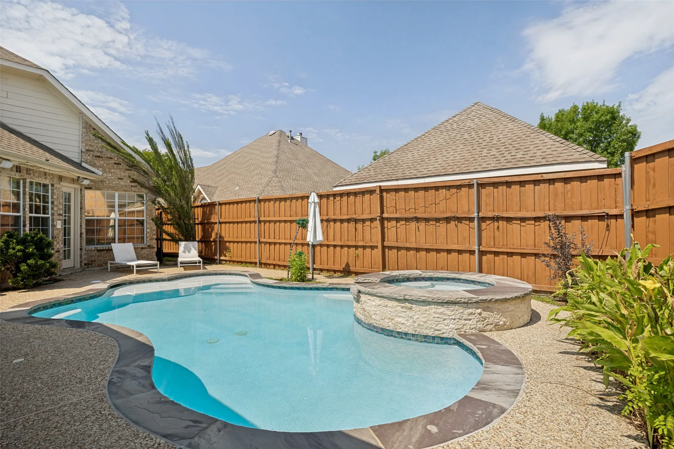 Pebble-finish patio with a freeform swimming pool, integrated spa, and privacy fencing