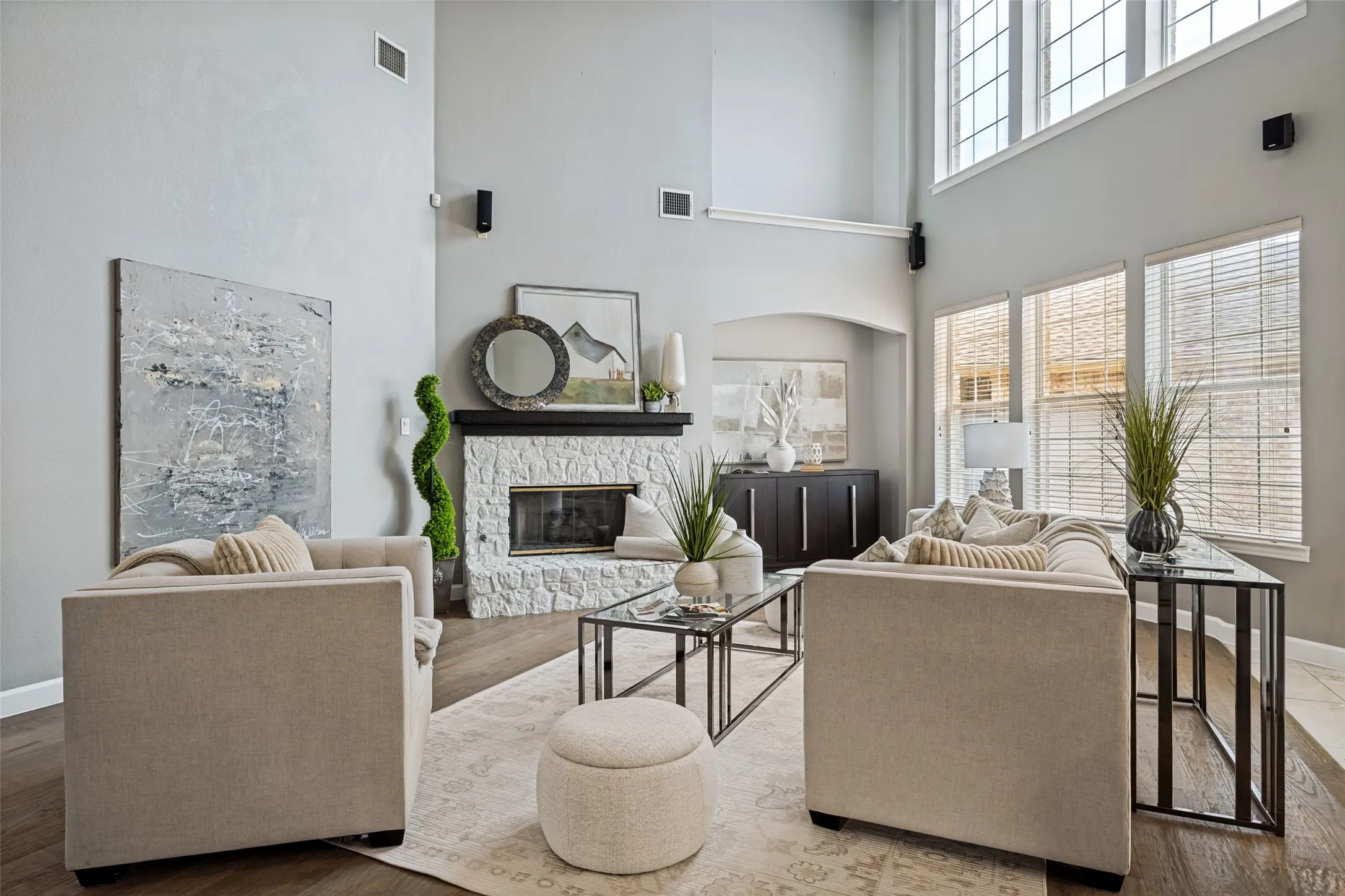 Two-story ceiling, stone-clad fireplace, dark wood-finish flooring, and multiple windows with blinds