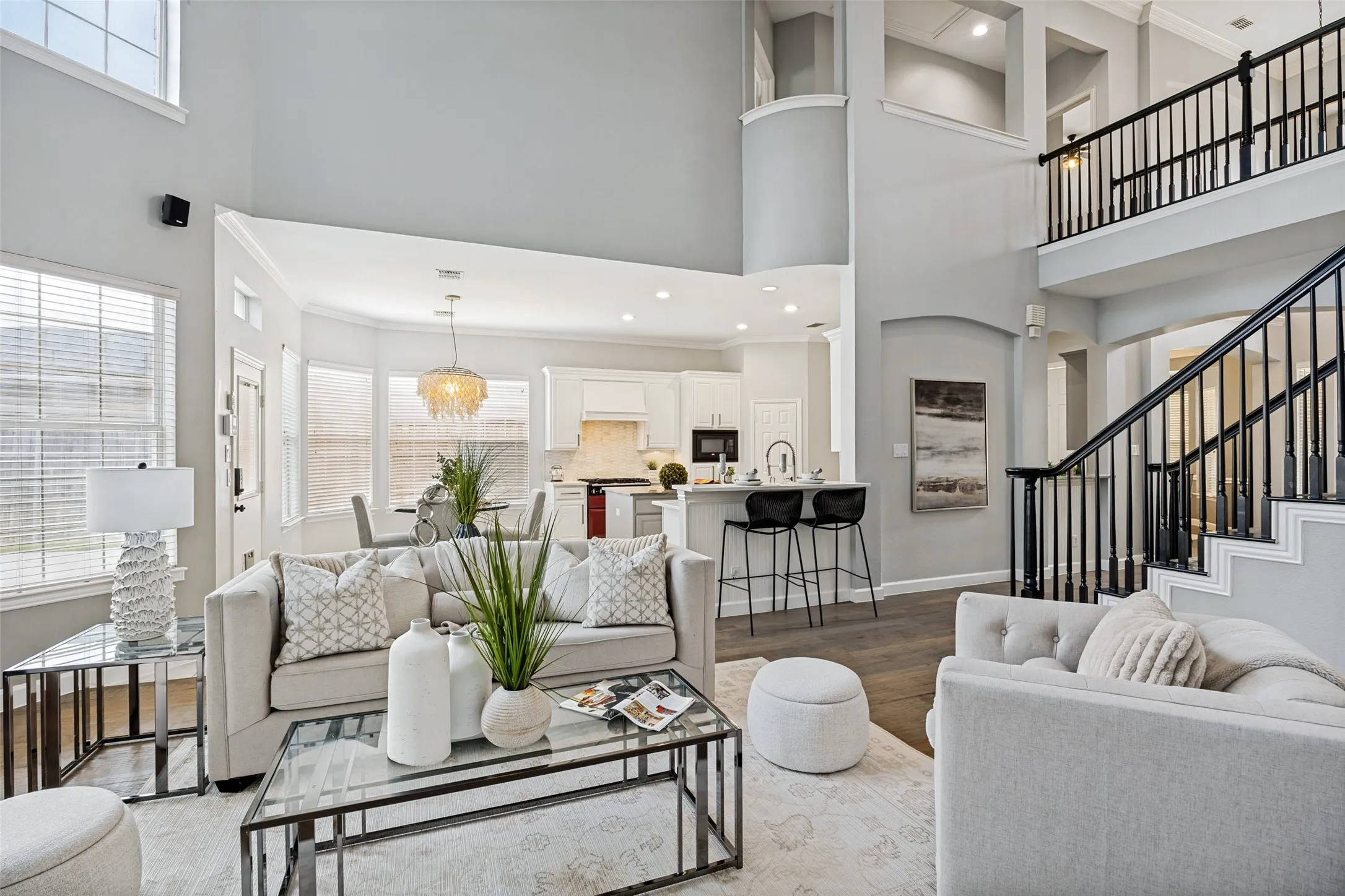 Two-story living area with high ceilings, dark wood-finish flooring, and a grand staircase featuring dark iron balusters