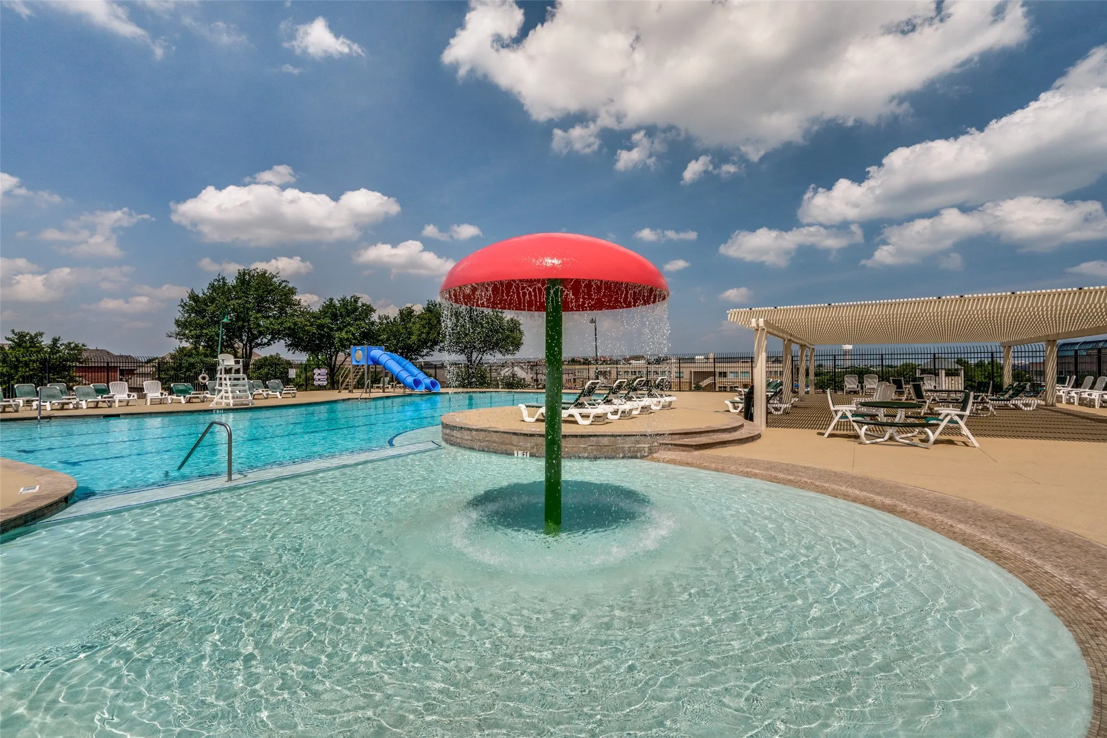 Resort-Style Community Pool featuring a shallow splash pad with integrated umbrella shade, Olympic-length lap lane with diving board, and expansive sun deck with lounge seating