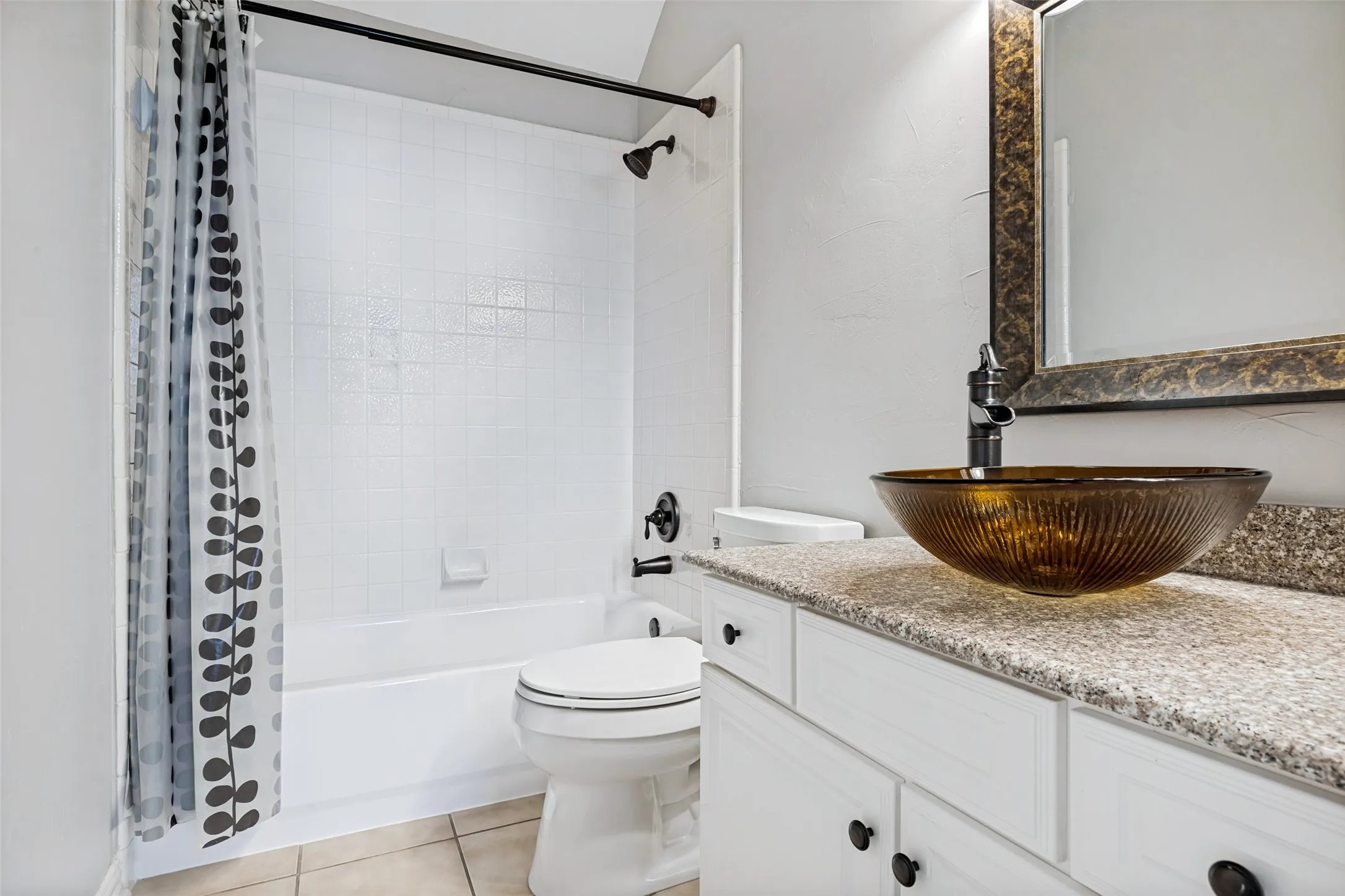 White vanity with dark hardware, vessel sink, and an integrated bathtub with a shower