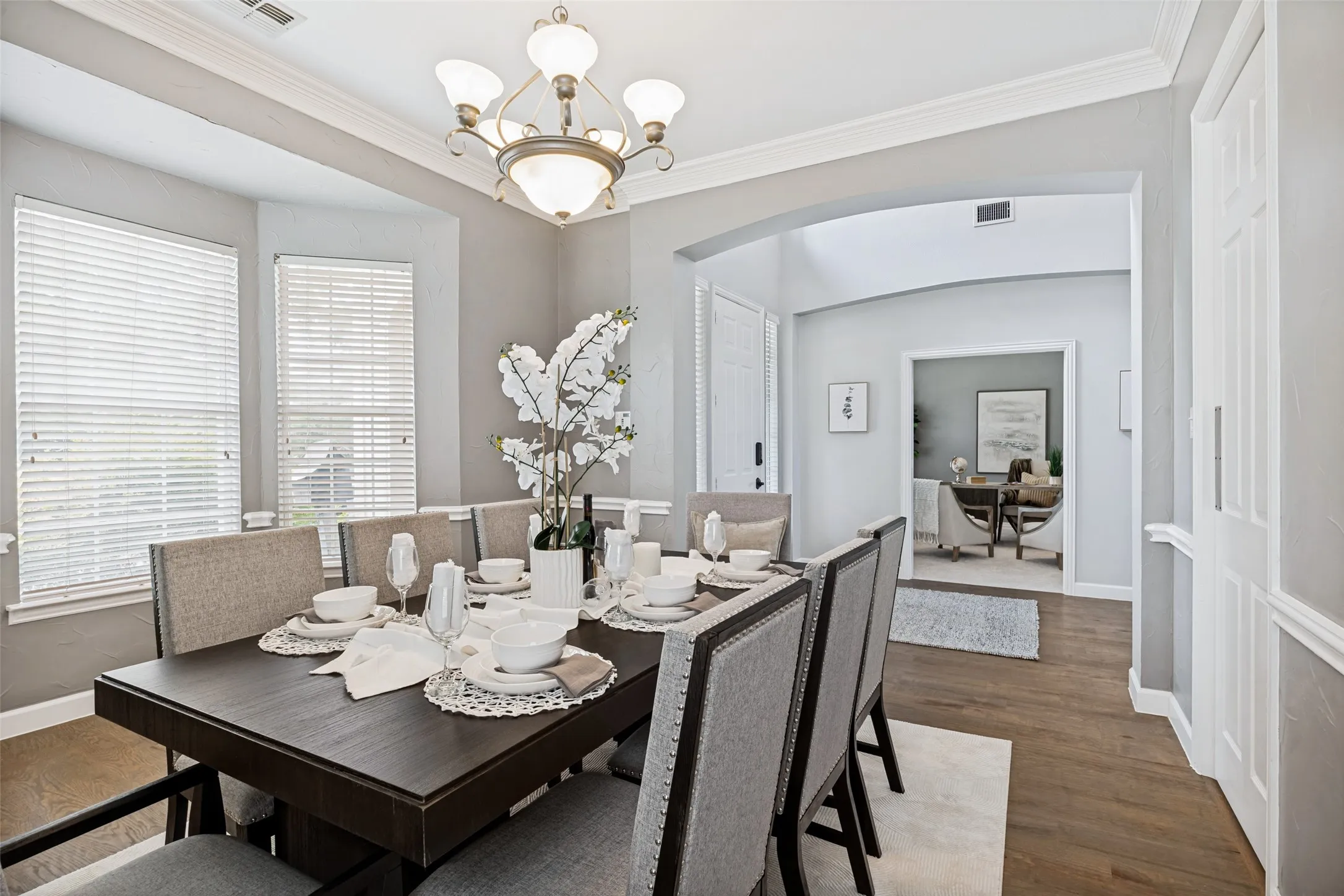 Dining area with bay windows, wood-finish flooring, a decorative chandelier, crown molding, and an arched entryway