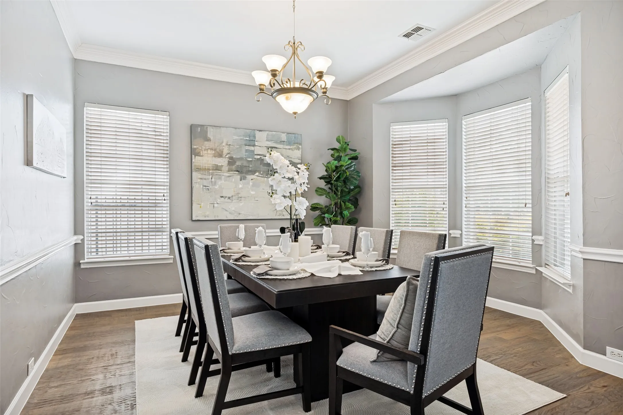 Dining space with wood-finish flooring, crown molding, and a bay window featuring three windows