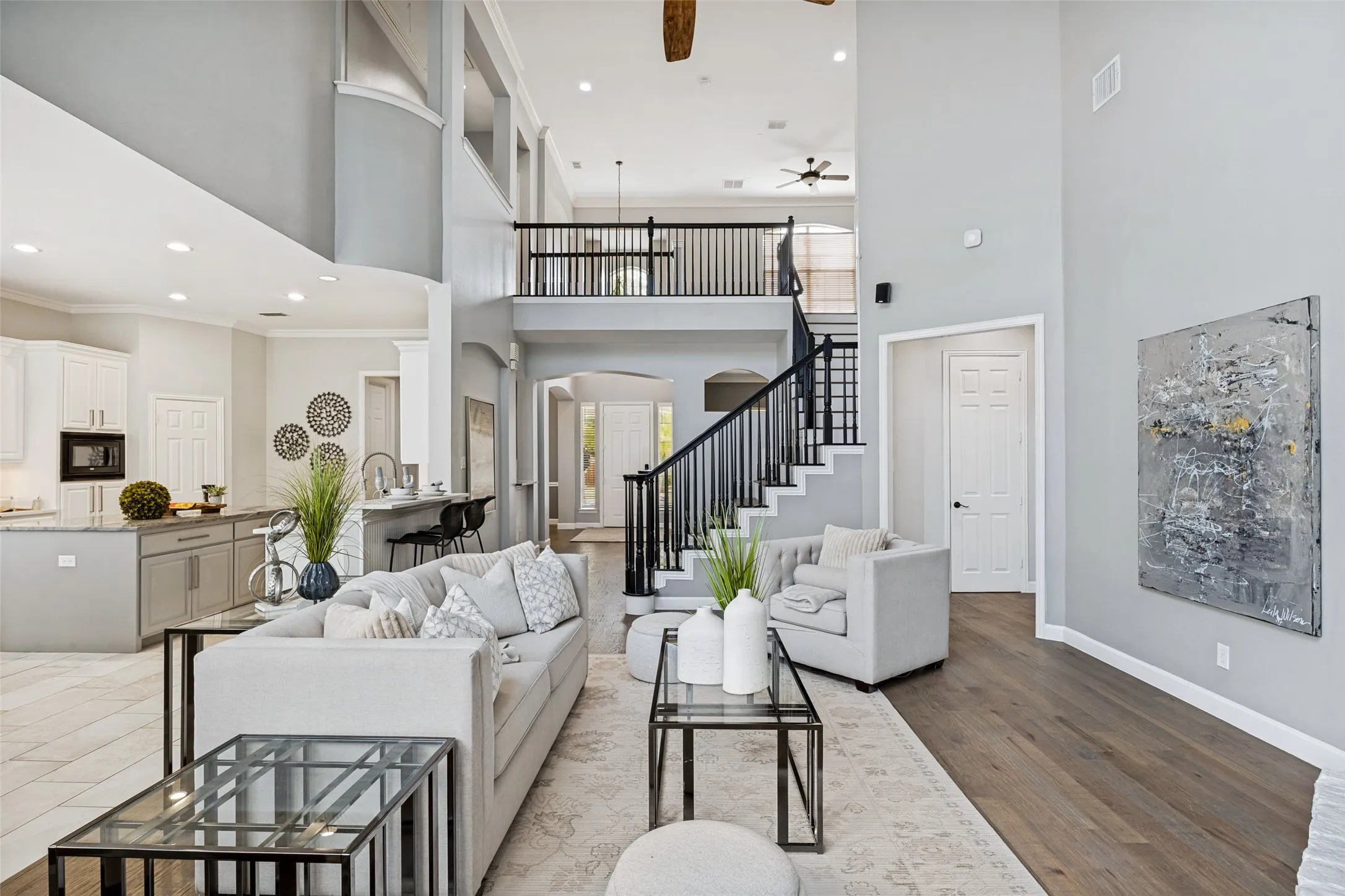 Two-story living area with high ceilings, an open-tread staircase with dark balusters, an upper-level balcony, and wood-finish flooring