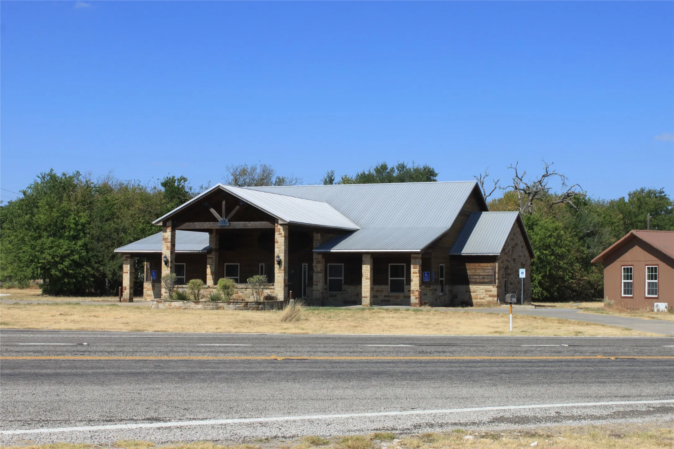 Stone and wood-finish exterior featuring a metal roof, covered entry with exposed beams, and a separate structure