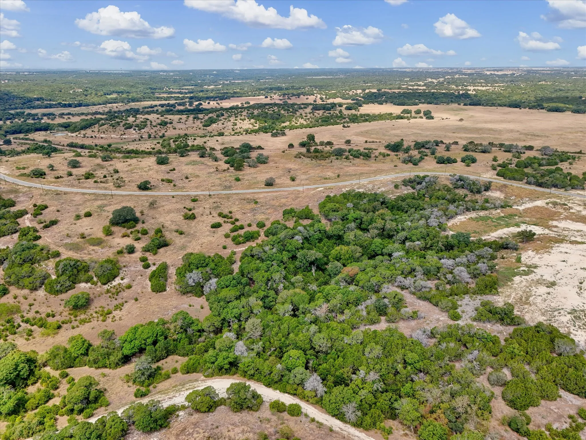 Expansive natural landscape featuring varied terrain, scattered clusters of trees, and a visible road