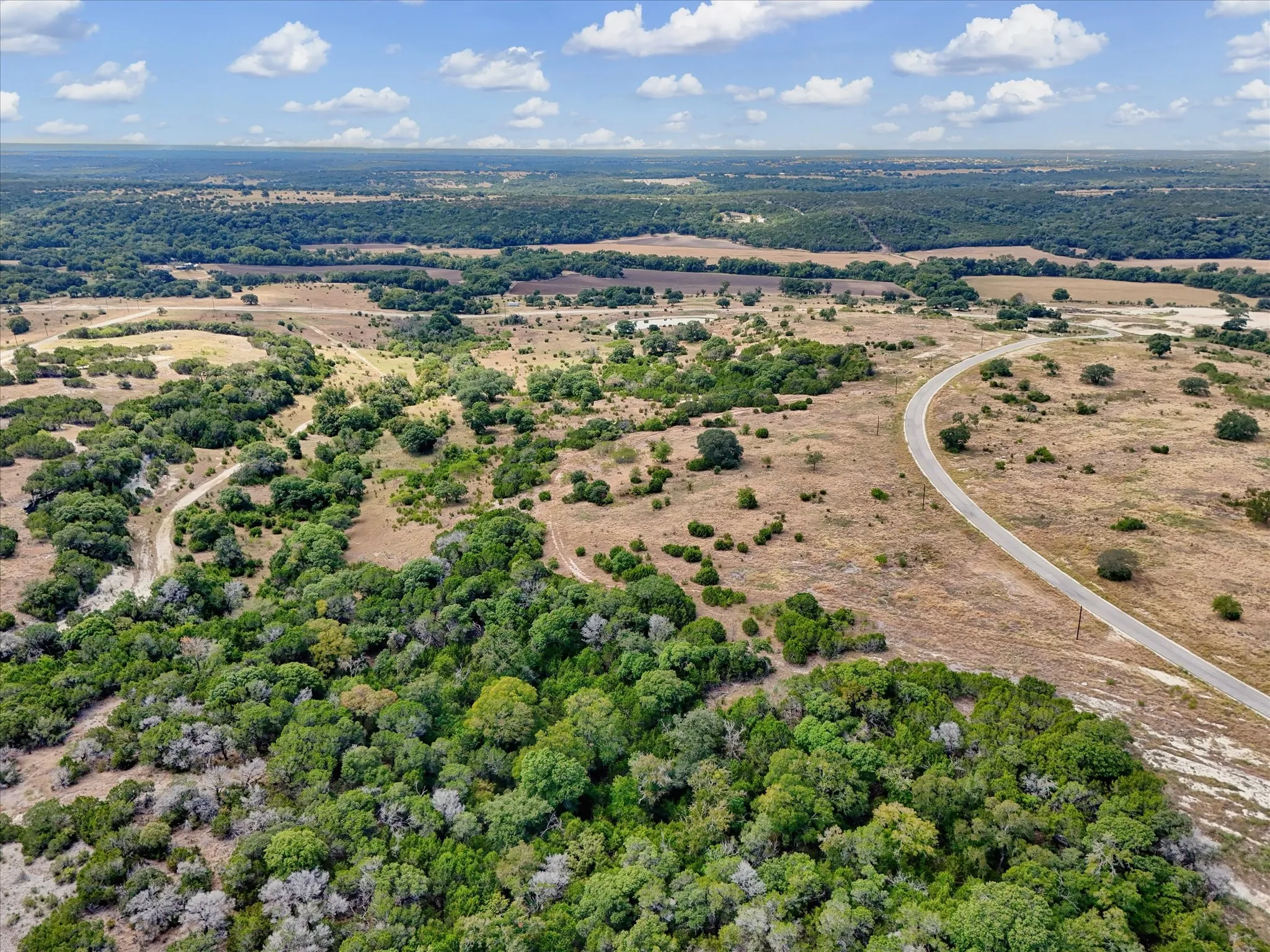 Expansive property featuring varied terrain, mature trees, open land, and a paved road