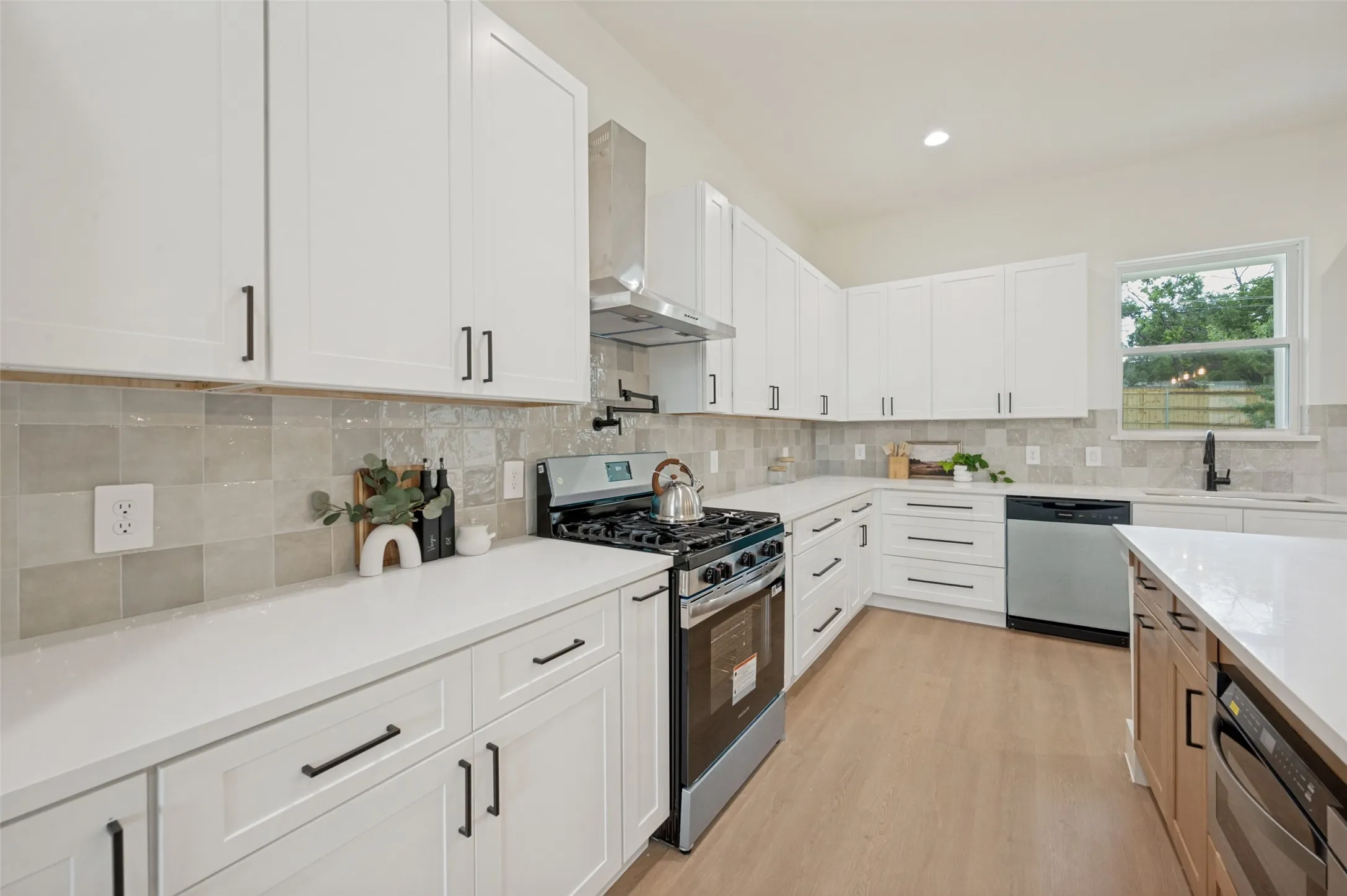 Contemporary kitchen featuring white cabinetry, light-toned countertops, a stainless steel range with a ventilation hood, and light-colored tile backsplash