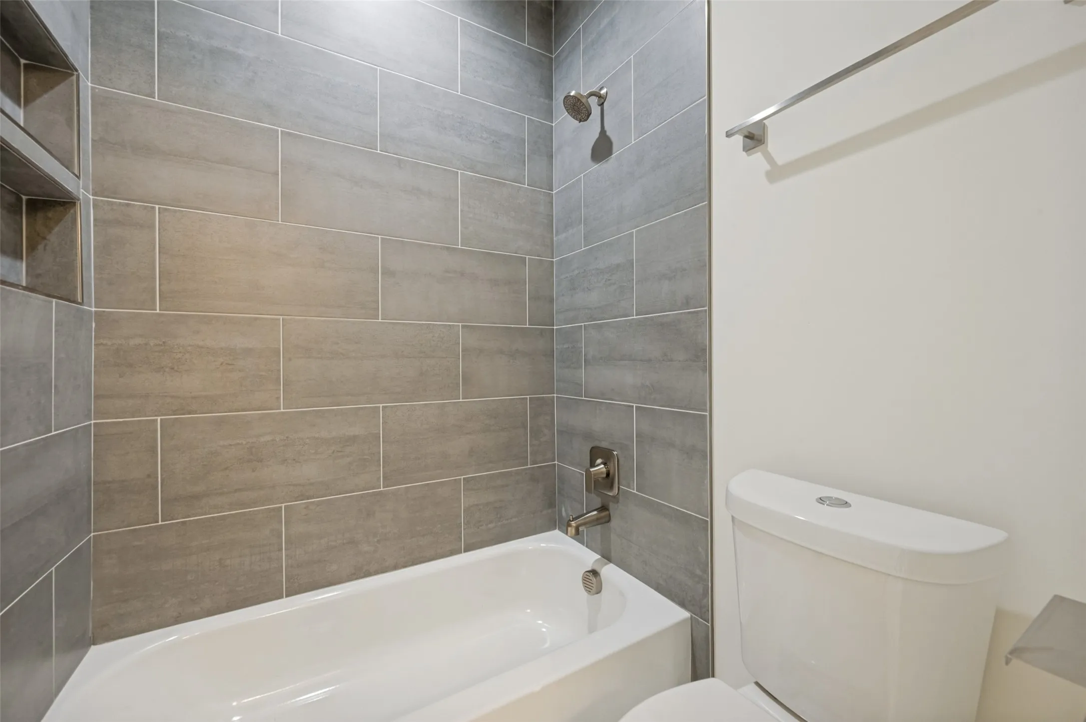 Bathtub with integrated shower, subway tile surround, recessed shower niche, and brushed nickel fixtures