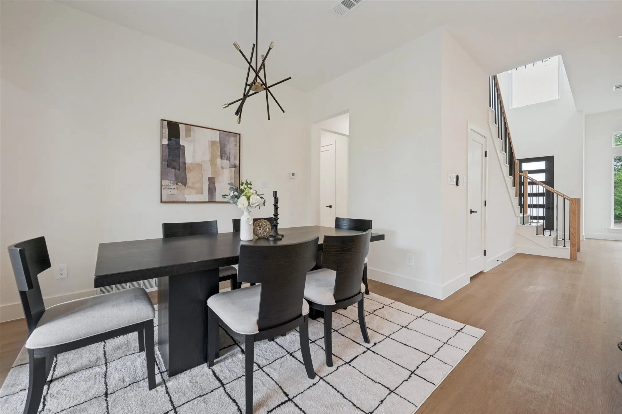 Open-concept living area featuring a modern chandelier, light wood-finish flooring, and a contemporary staircase with wood and metal railing