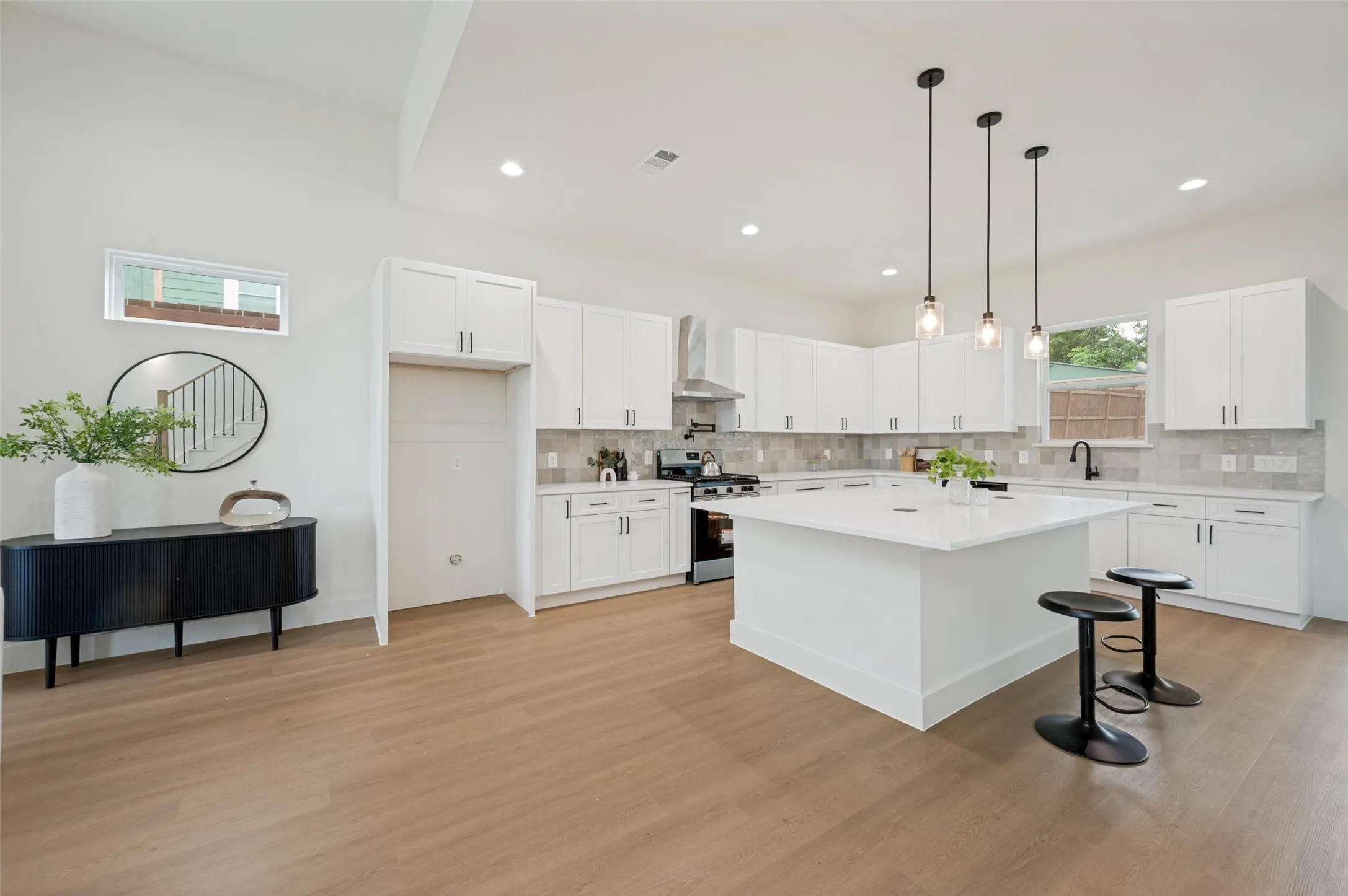 Spacious kitchen featuring an expansive island with a light-toned countertop, white cabinetry with dark hardware, and a tile backsplash