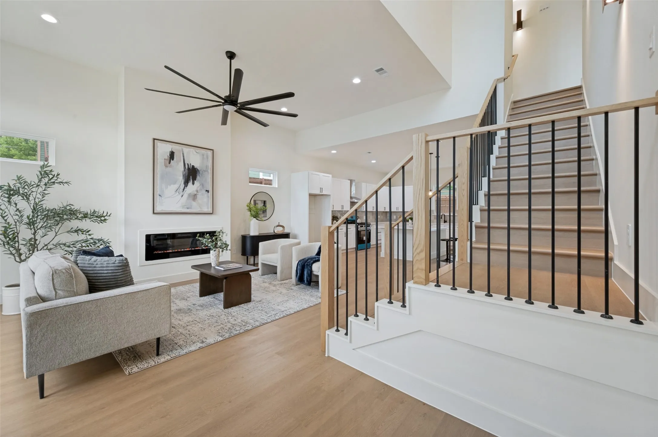 Vaulted ceiling, built-in linear fireplace, wood-finish flooring, staircase with black metal balusters and wood handrail, and recessed lighting