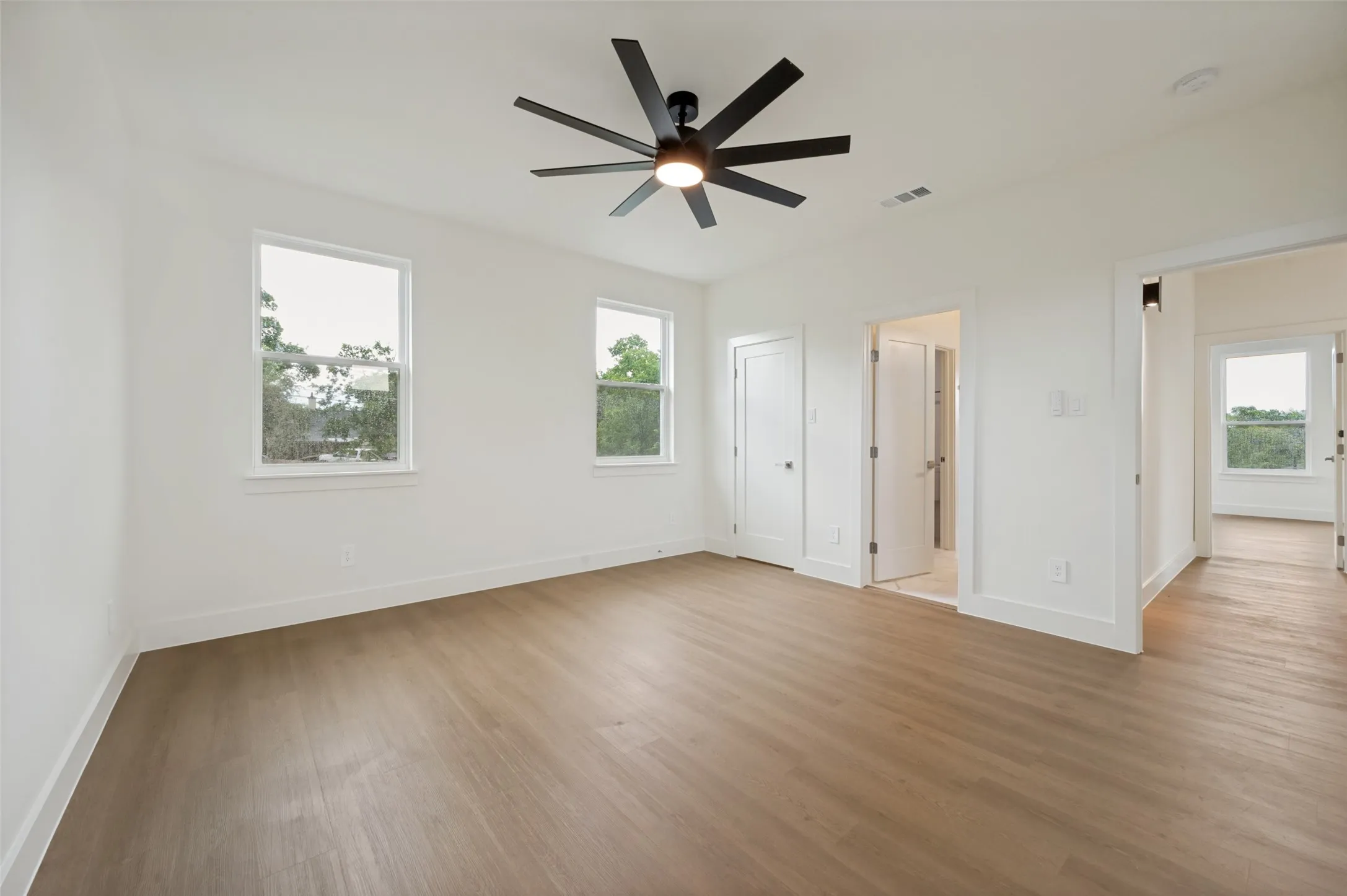 Light-filled interior featuring two windows, wood-finish flooring, a modern ceiling fan, and white painted walls