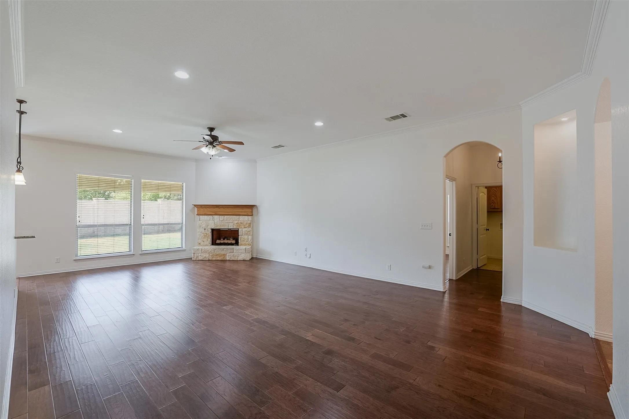 Hardwood-finish flooring, stone-clad fireplace with wood mantel, arched entryways, recessed lighting, and a ceiling fan